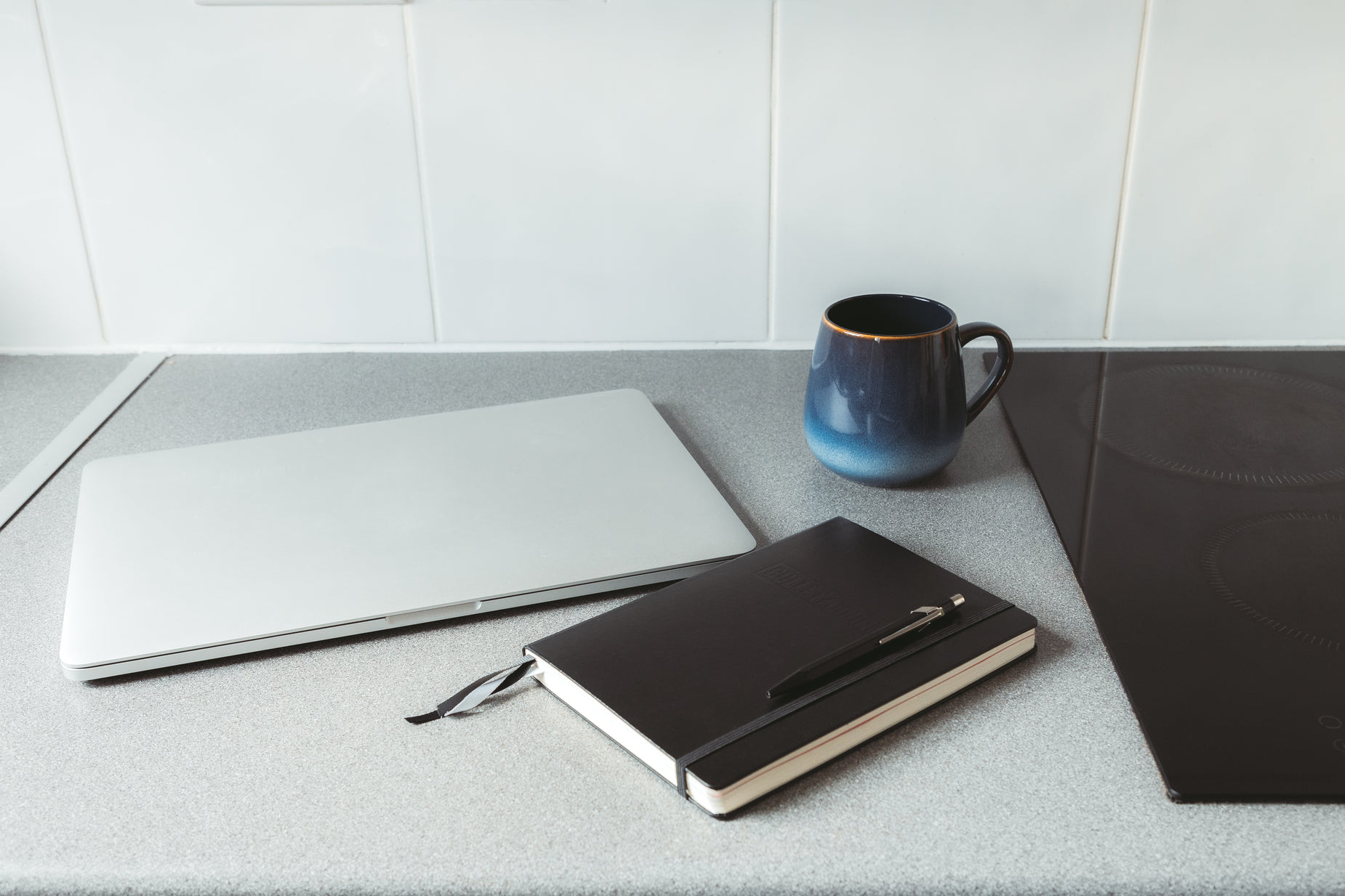 a mug and notebook sitting on the counter next to a laptop computer