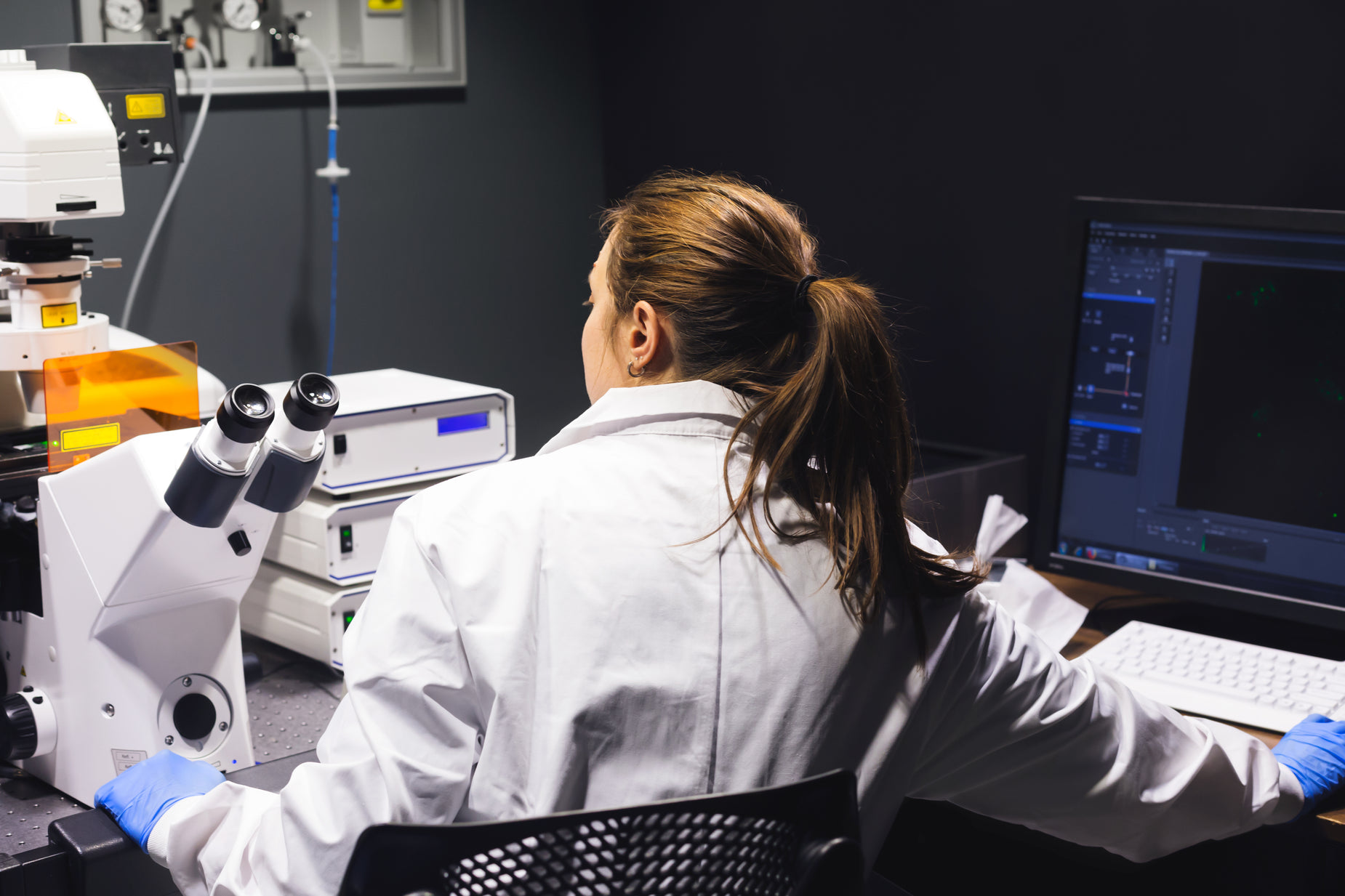 a woman in white lab coat looking through microscope