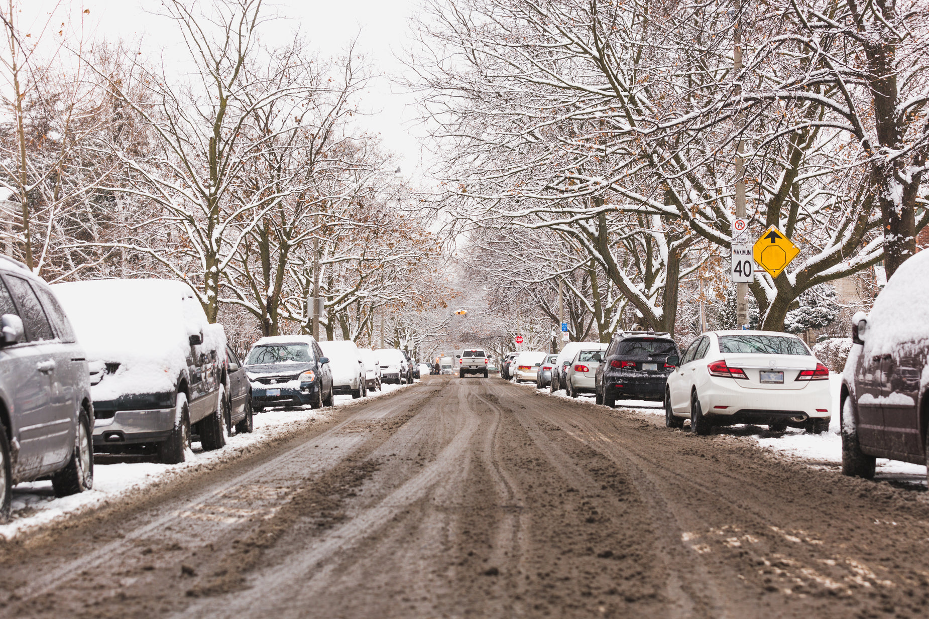 a bunch of cars are parked at a stop sign on the side of a road covered in snow