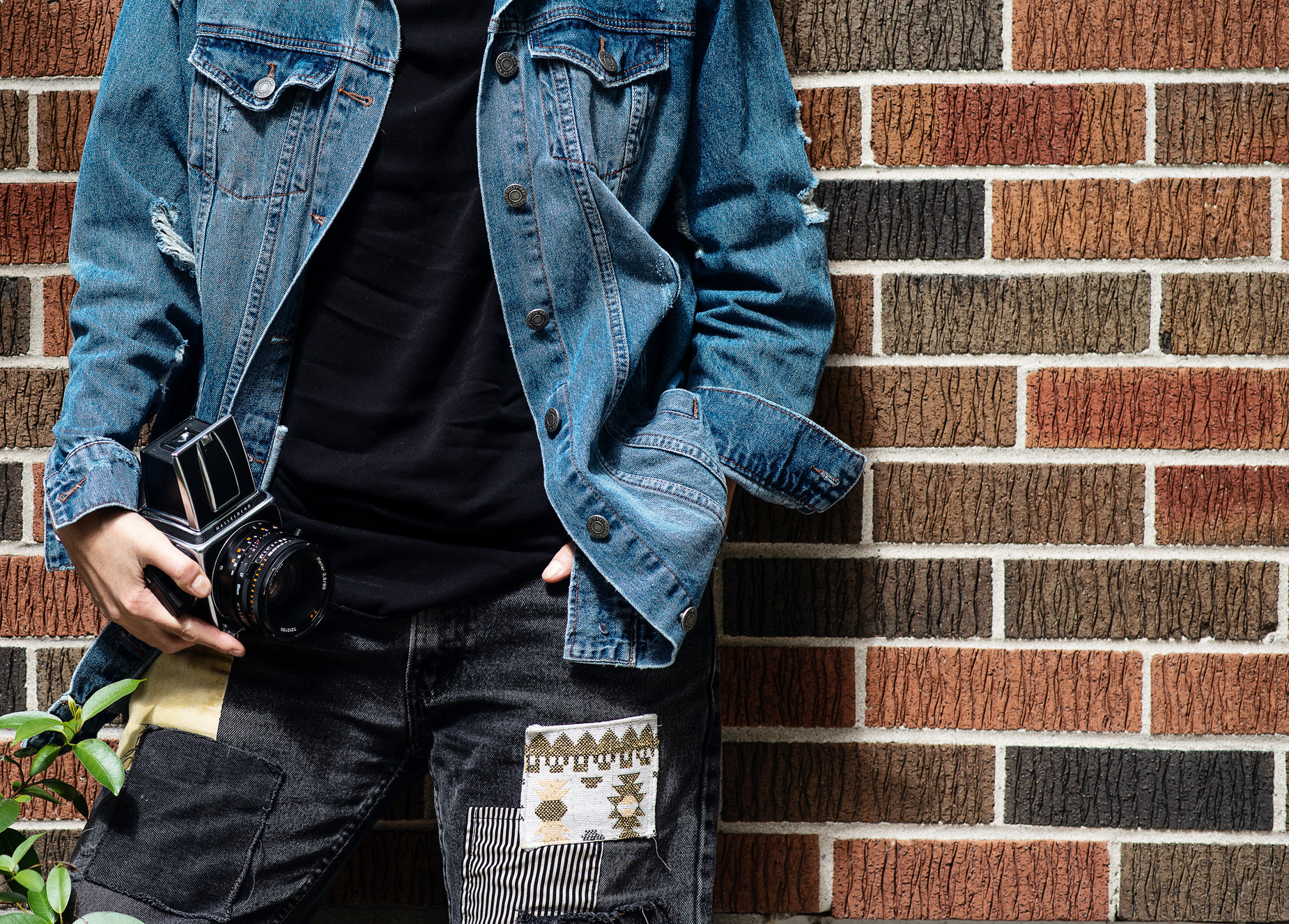 a man wearing a black shirt and jeans stands by a brick wall