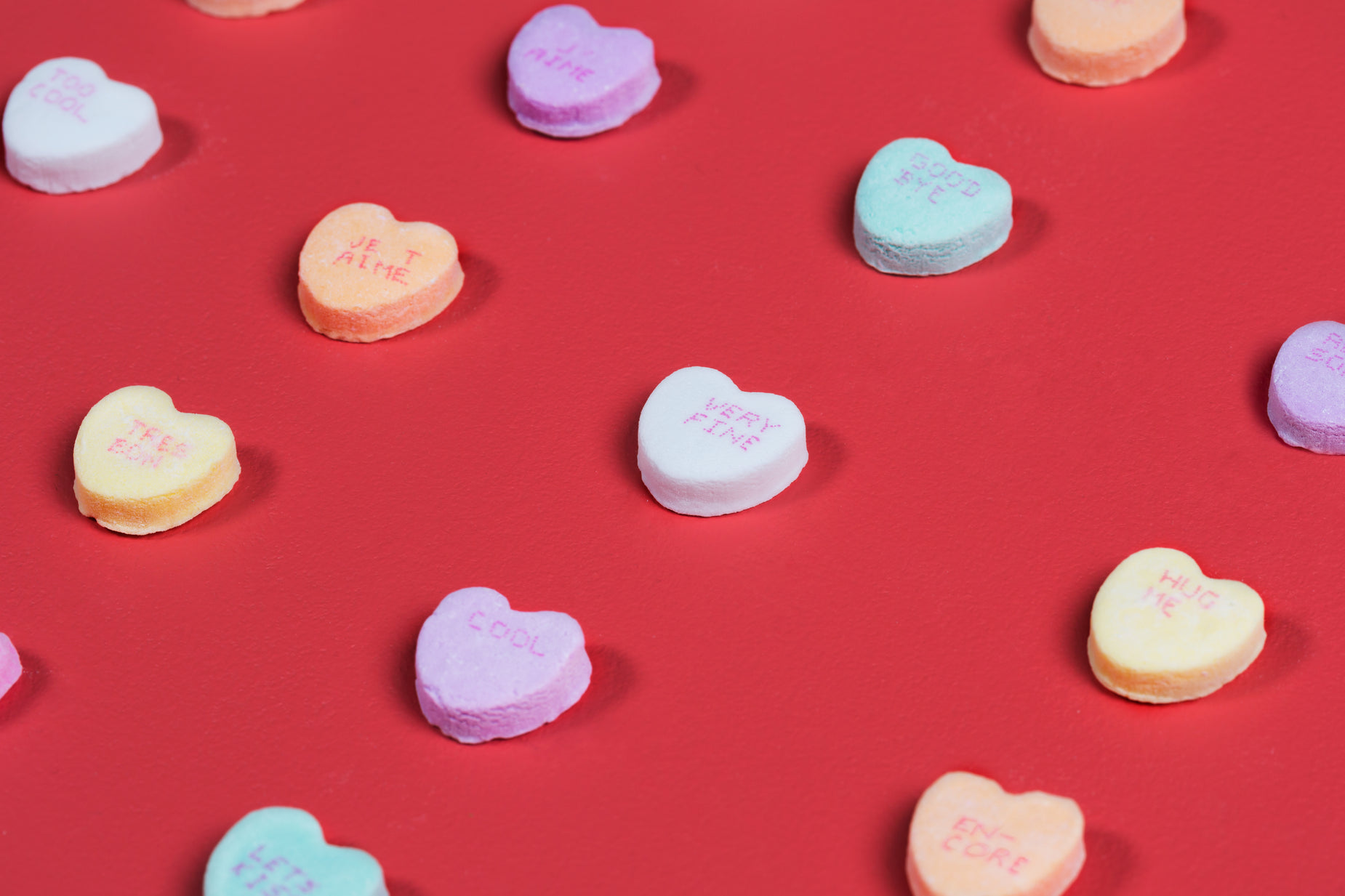 many small conversation hearts arranged on a red surface