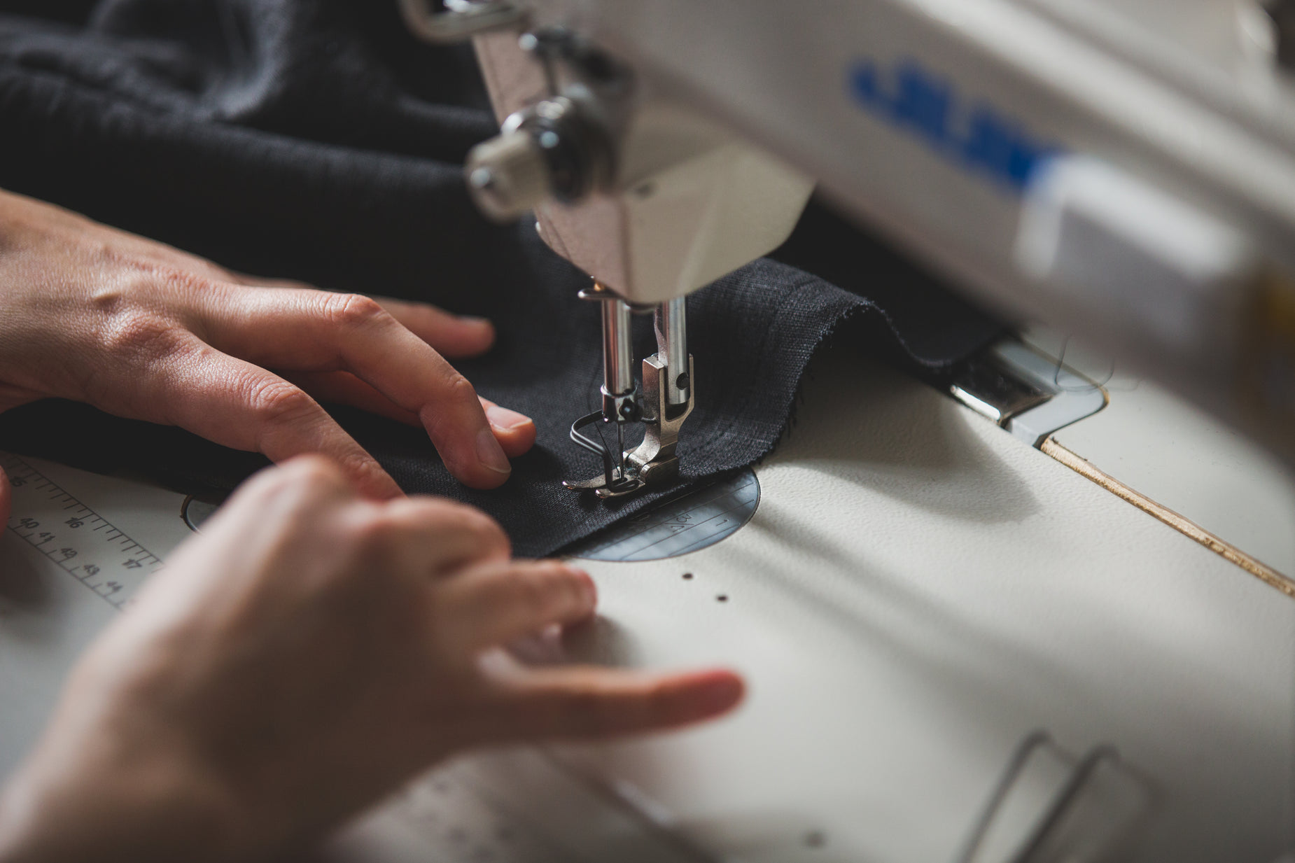 two hands operate the sewing machine while it is  fabric