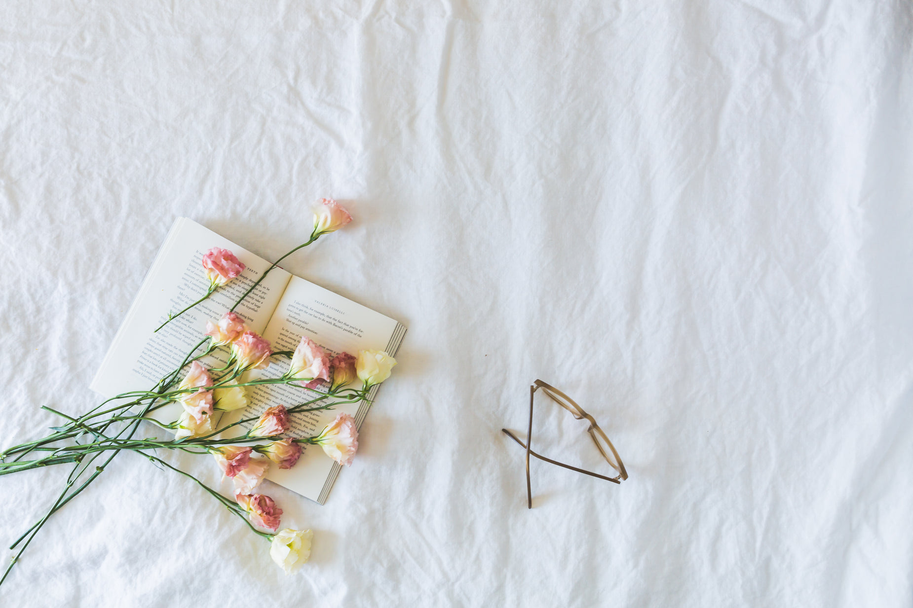 flowers are laying on top of an open book with glasses