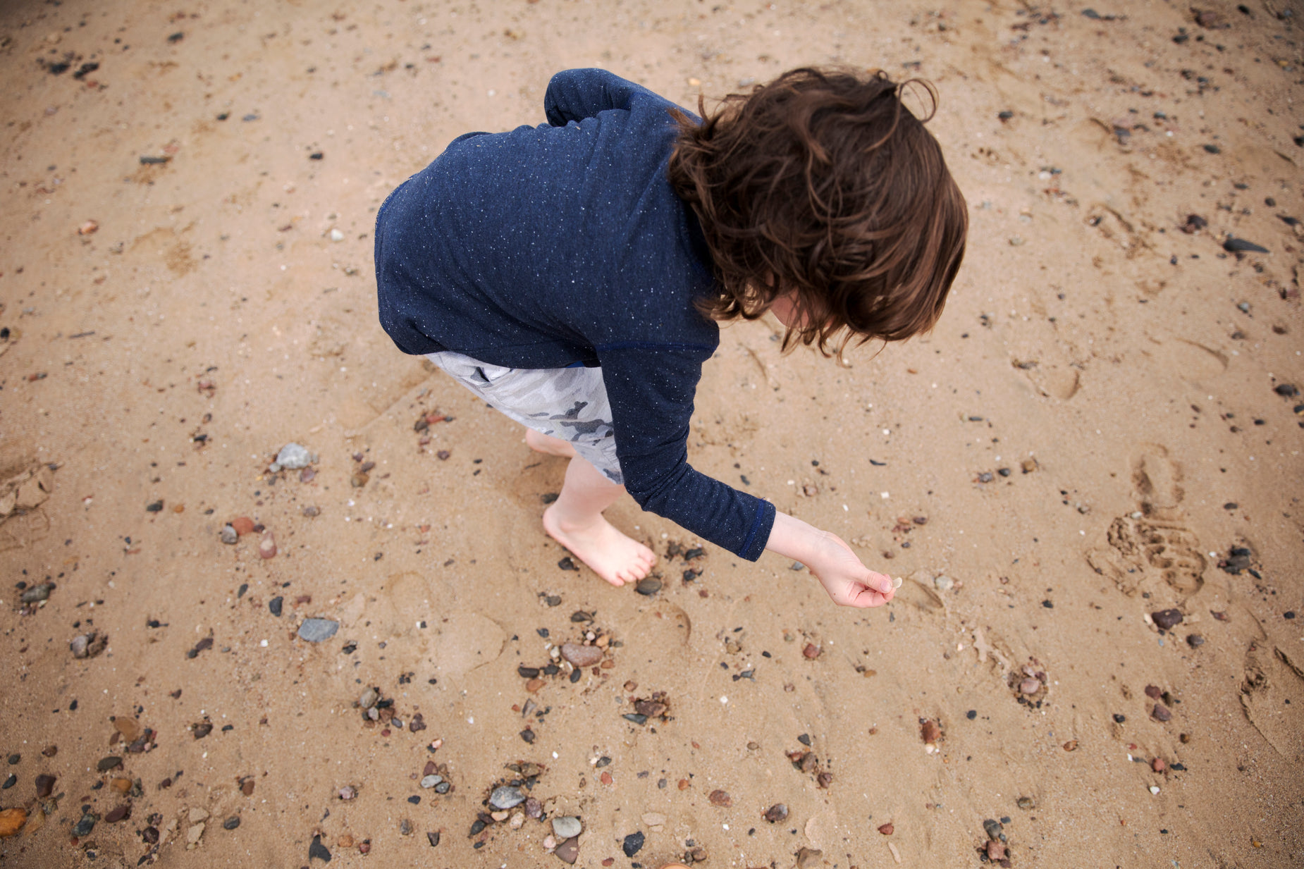 the small child is picking up the frisbee on the beach