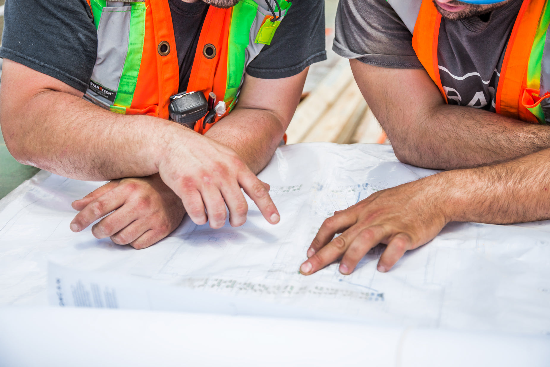 two men wearing orange safety vests are looking at blueprint