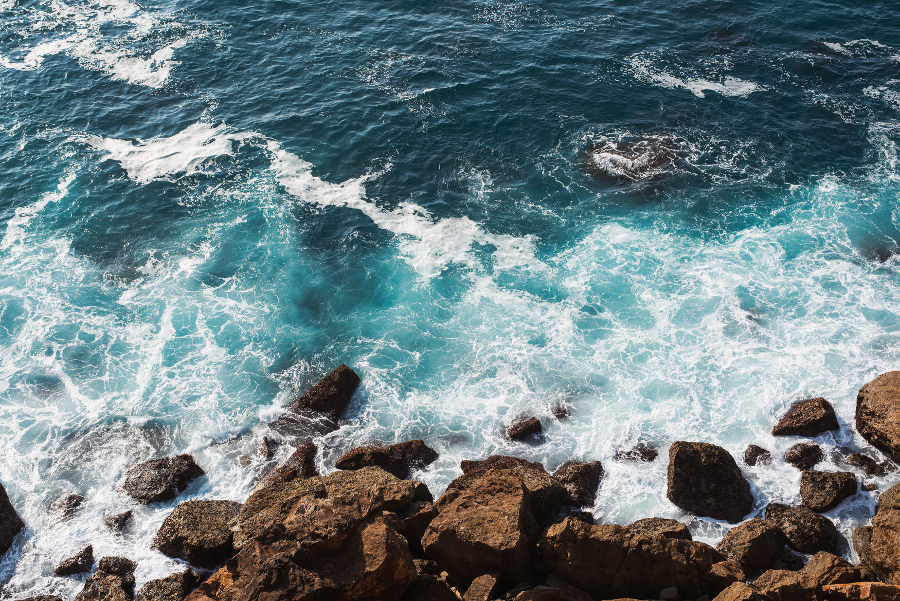 a couple of people sitting at the edge of the ocean on some rocks