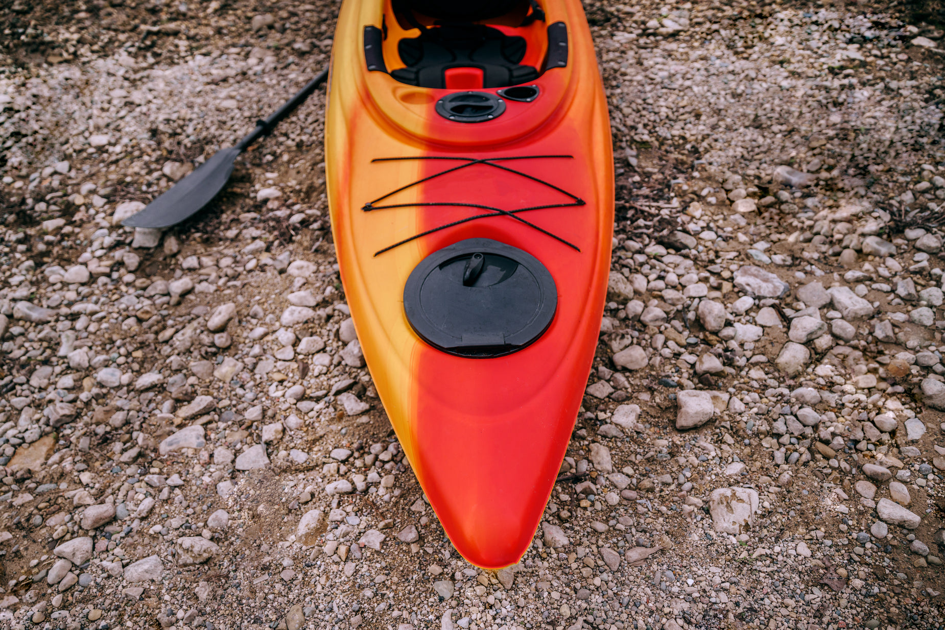 an orange kayak on the ground, surrounded by pebbles