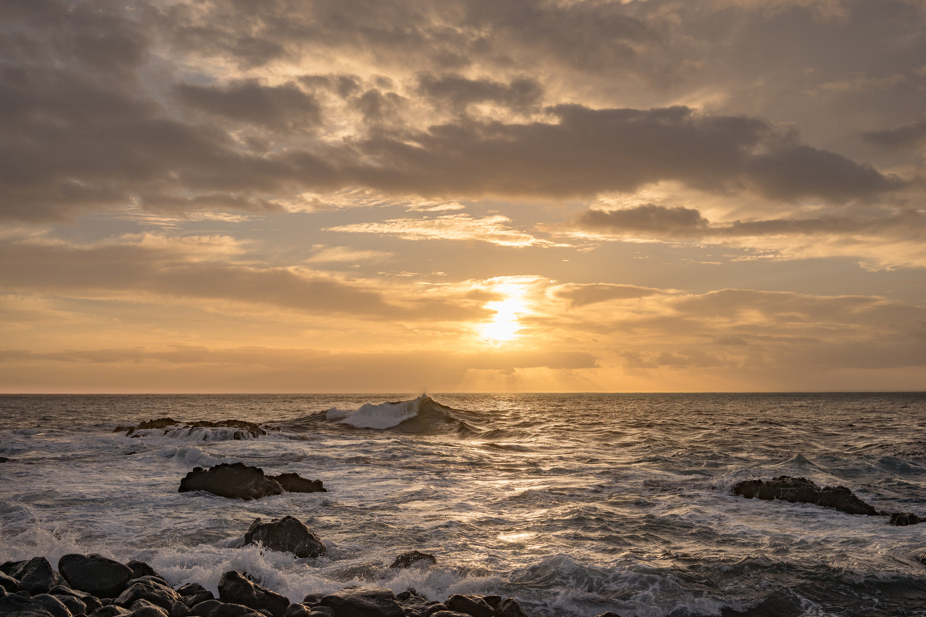 the sun is rising over the ocean with rocks in front of it