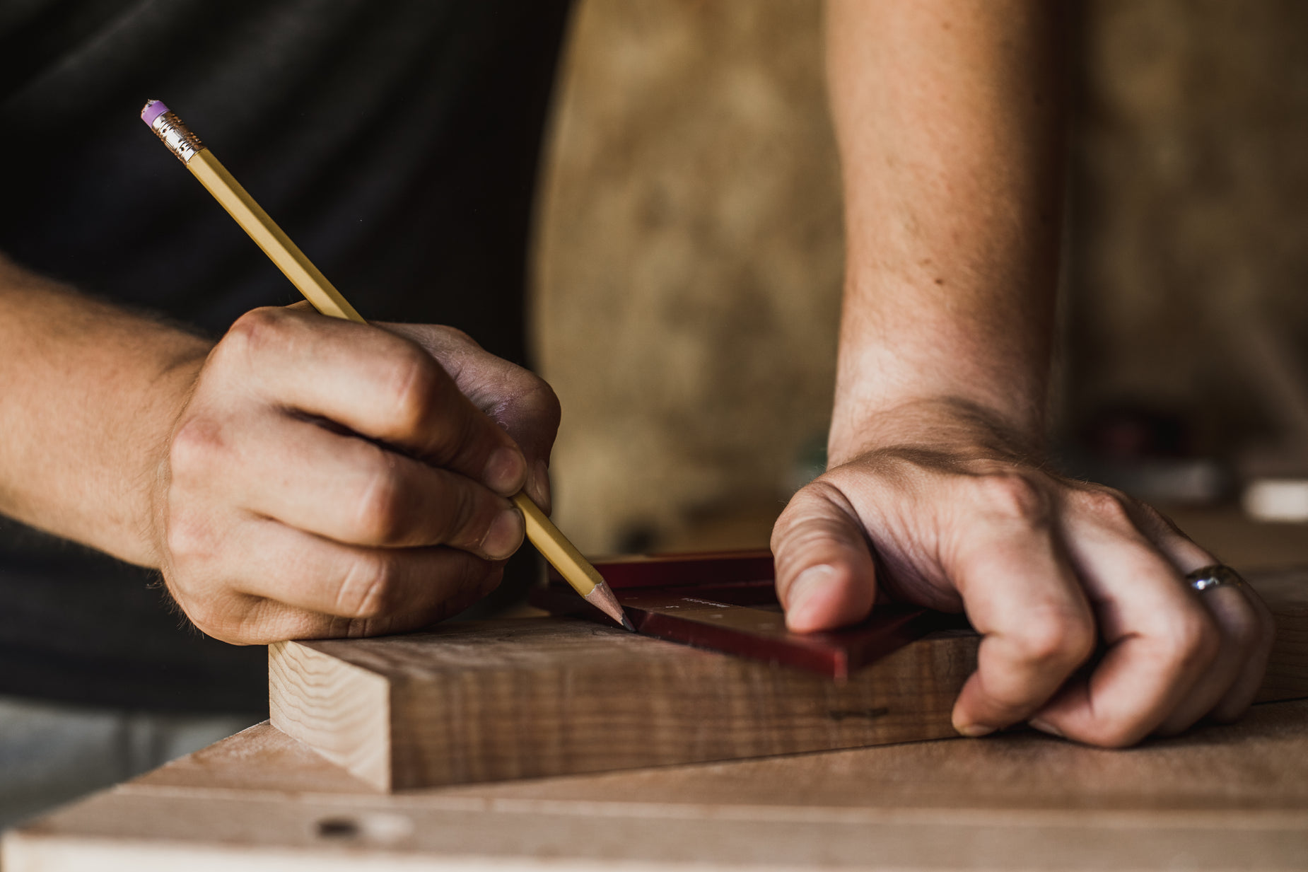 a man in a black shirt is writing on a piece of wood with a pencil