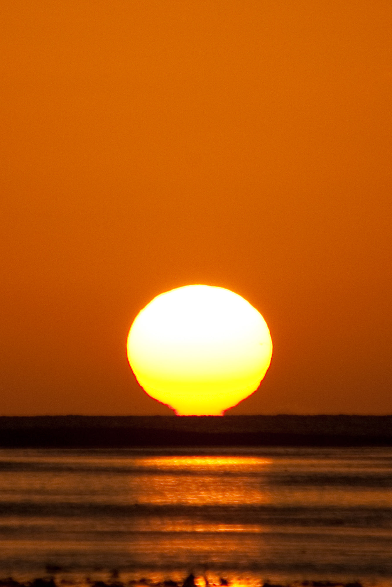 a yellow sunset over the ocean with an airplane flying through the sky