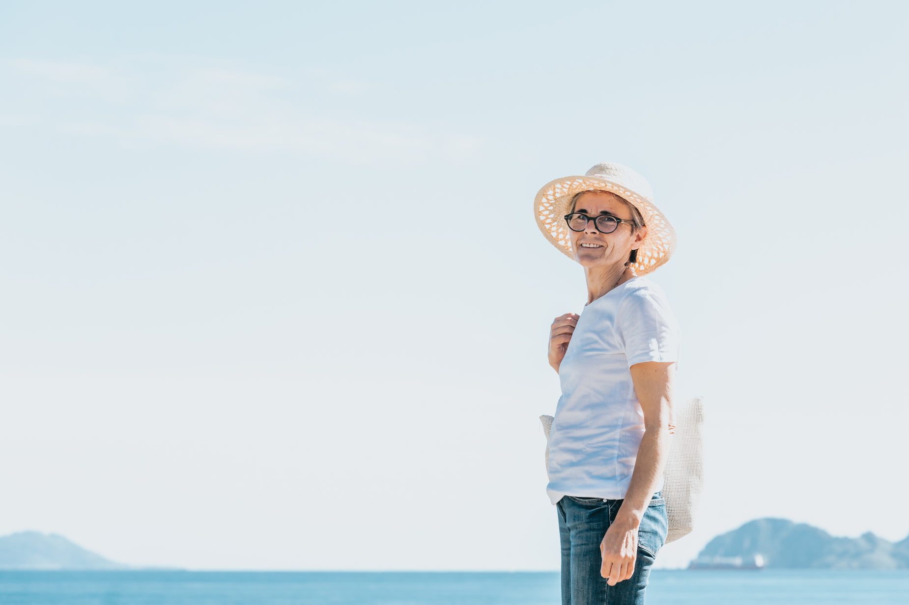 woman in a white shirt and hat standing on the beach