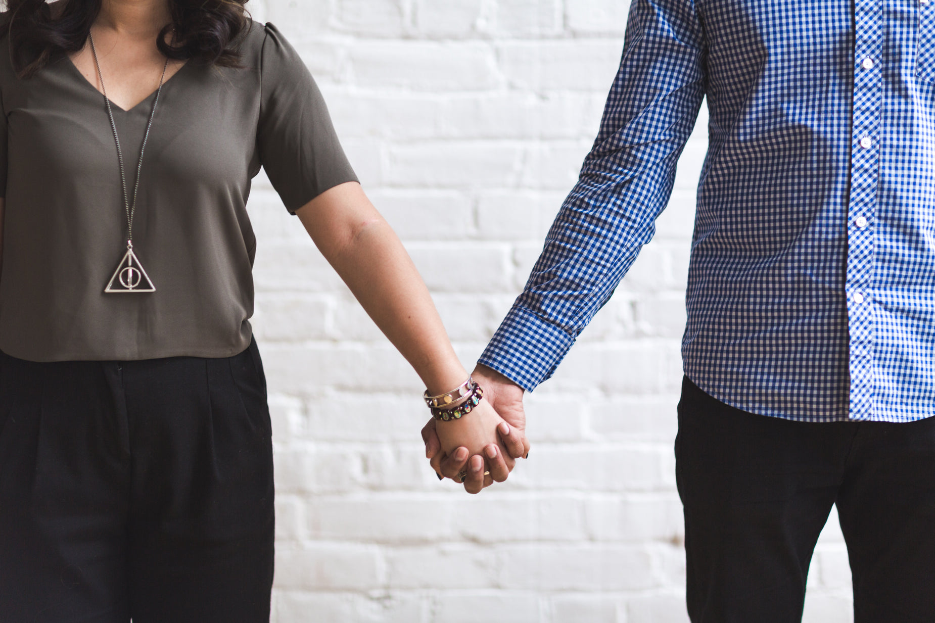 the couple hold hands while standing against a brick wall