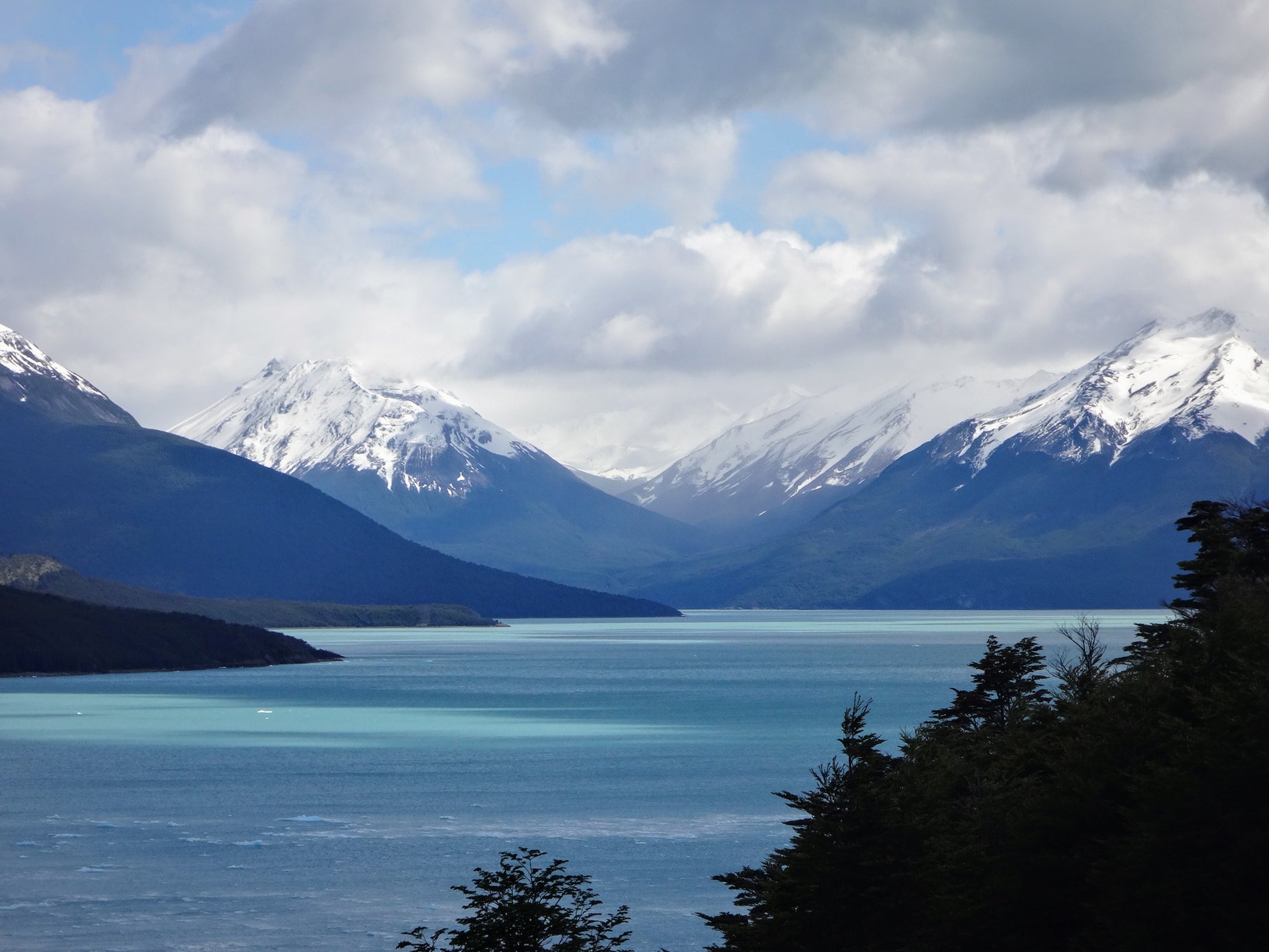 mountains with snow on top in the foreground and a lake with trees at the bottom