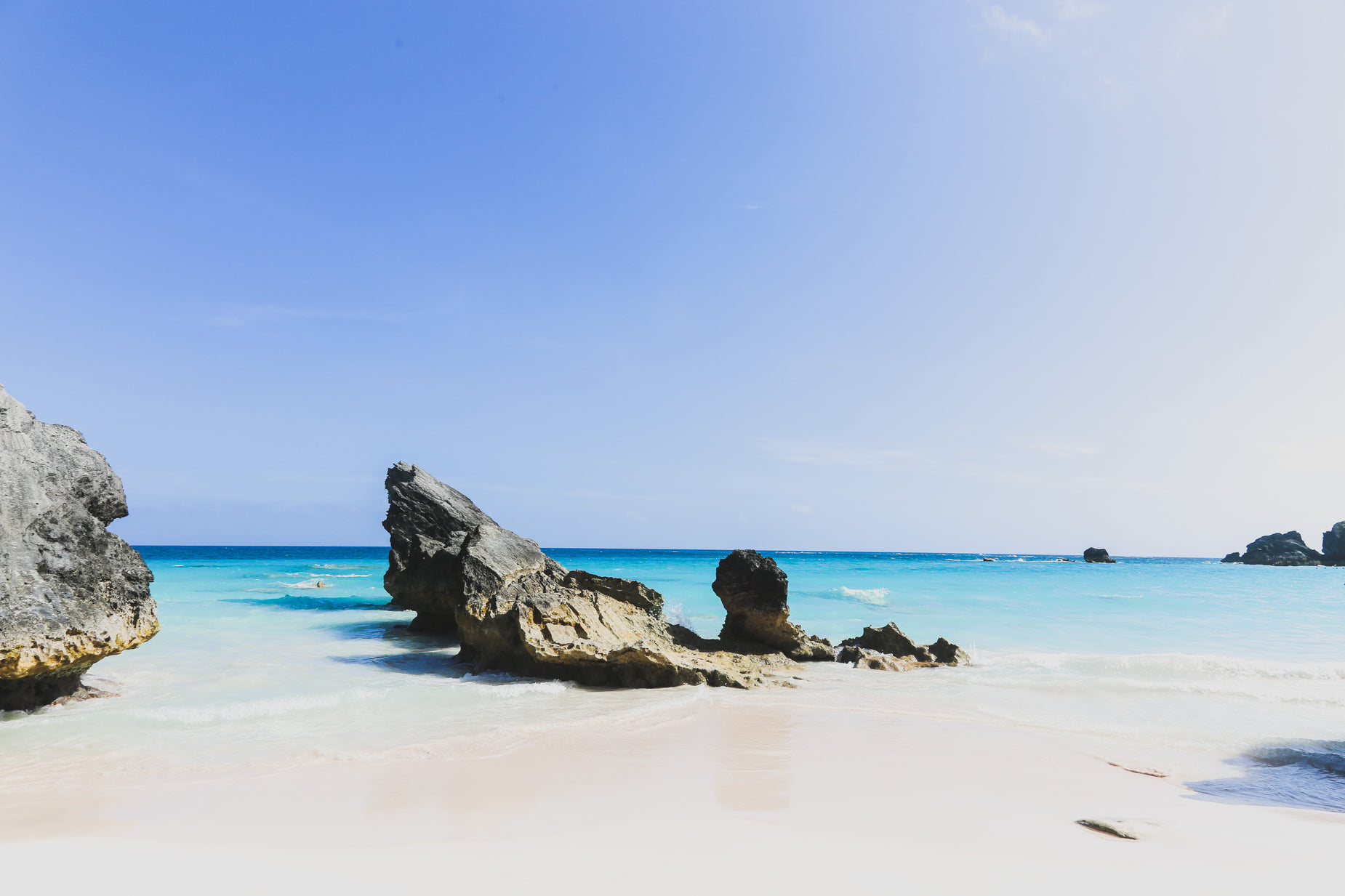 rocks on a white sandy beach at blue waters