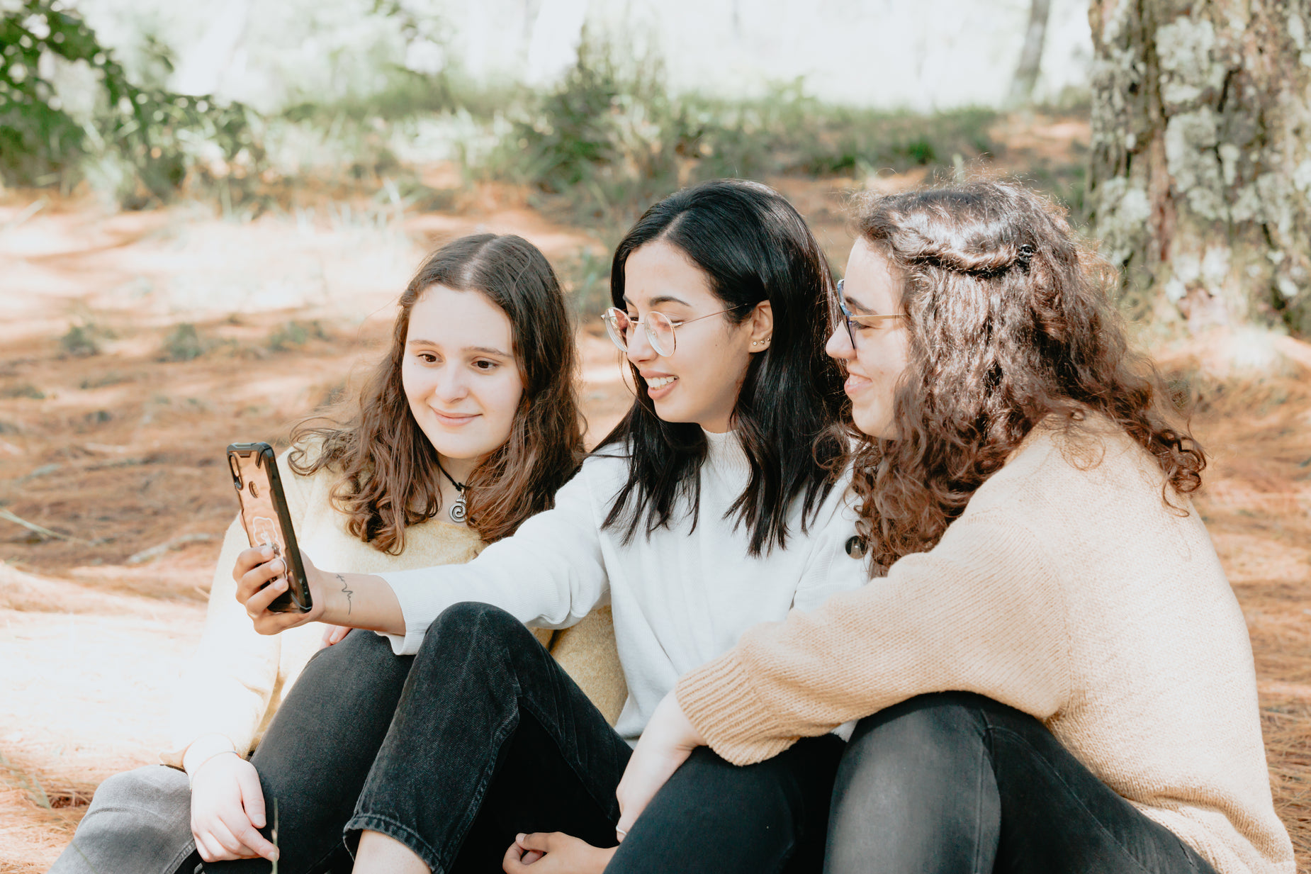 three women sitting together with a camera and a notebook