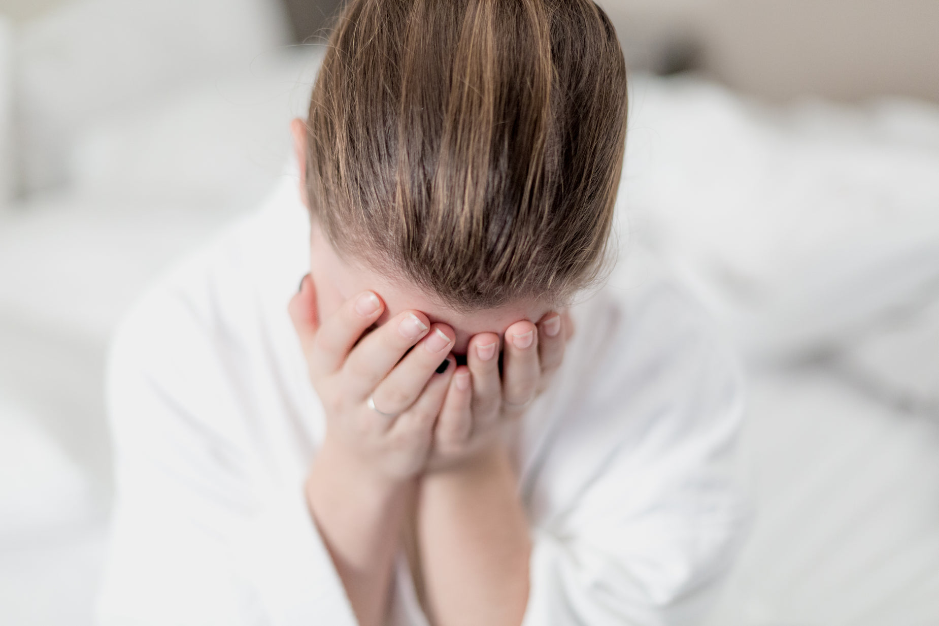 woman in white shirt covering her face with hands