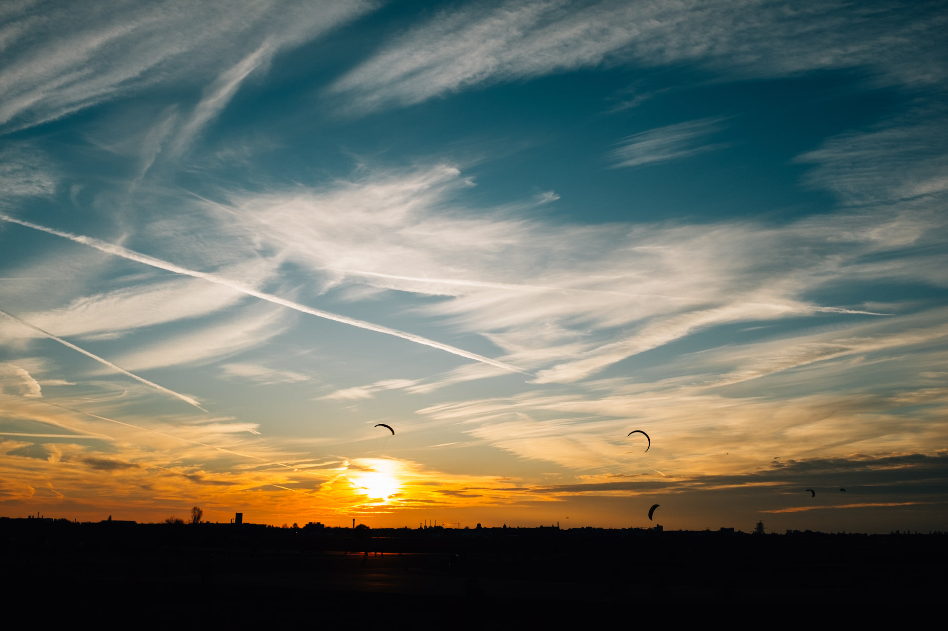 the sun is setting on the horizon behind some birds flying by