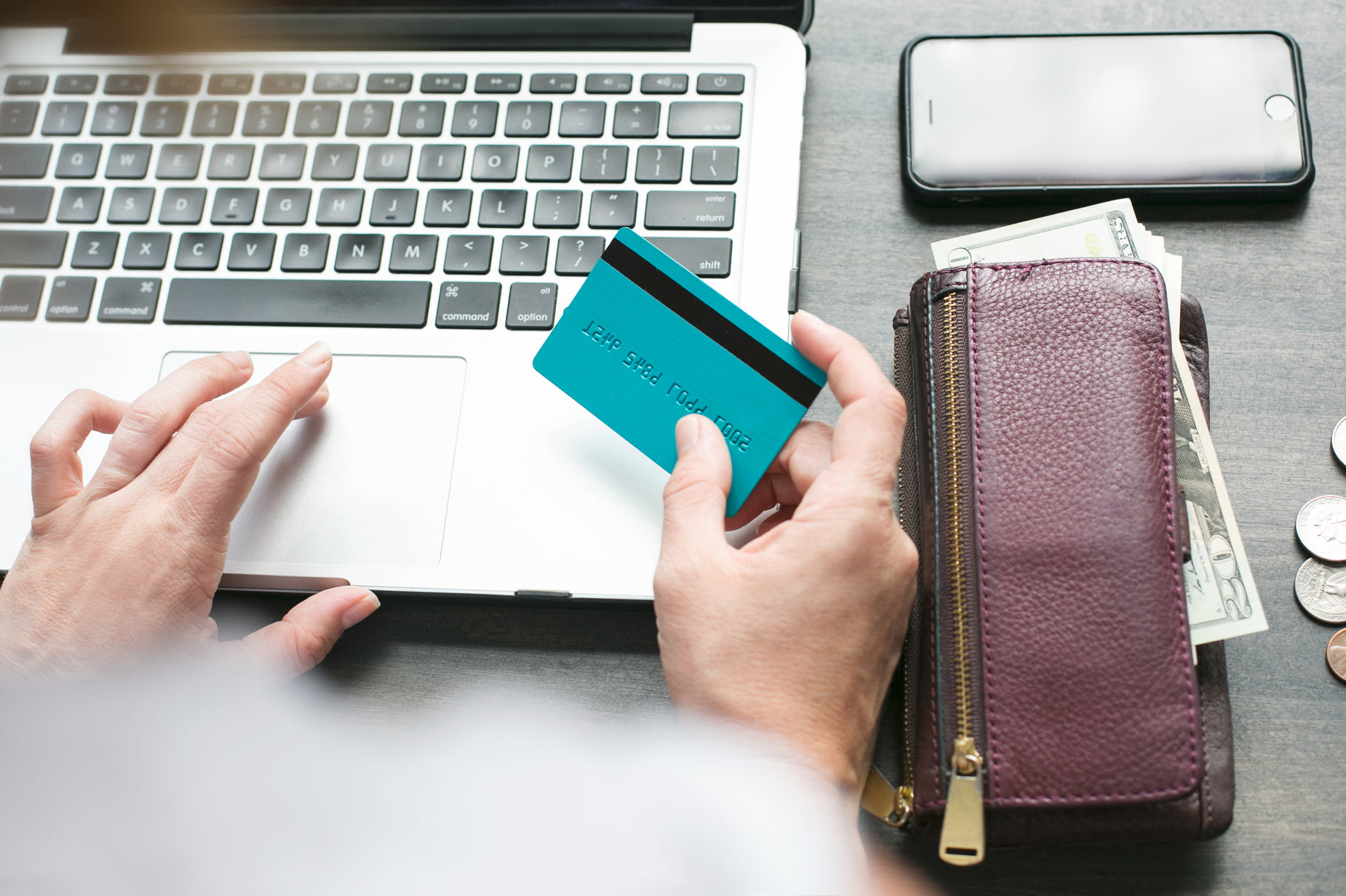 person using a laptop computer while holding onto credit cards