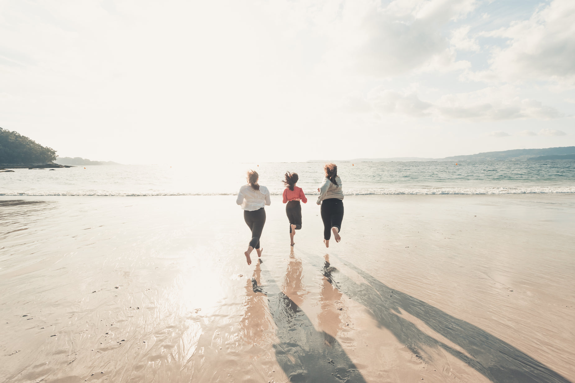 a trio of three women run along the beach