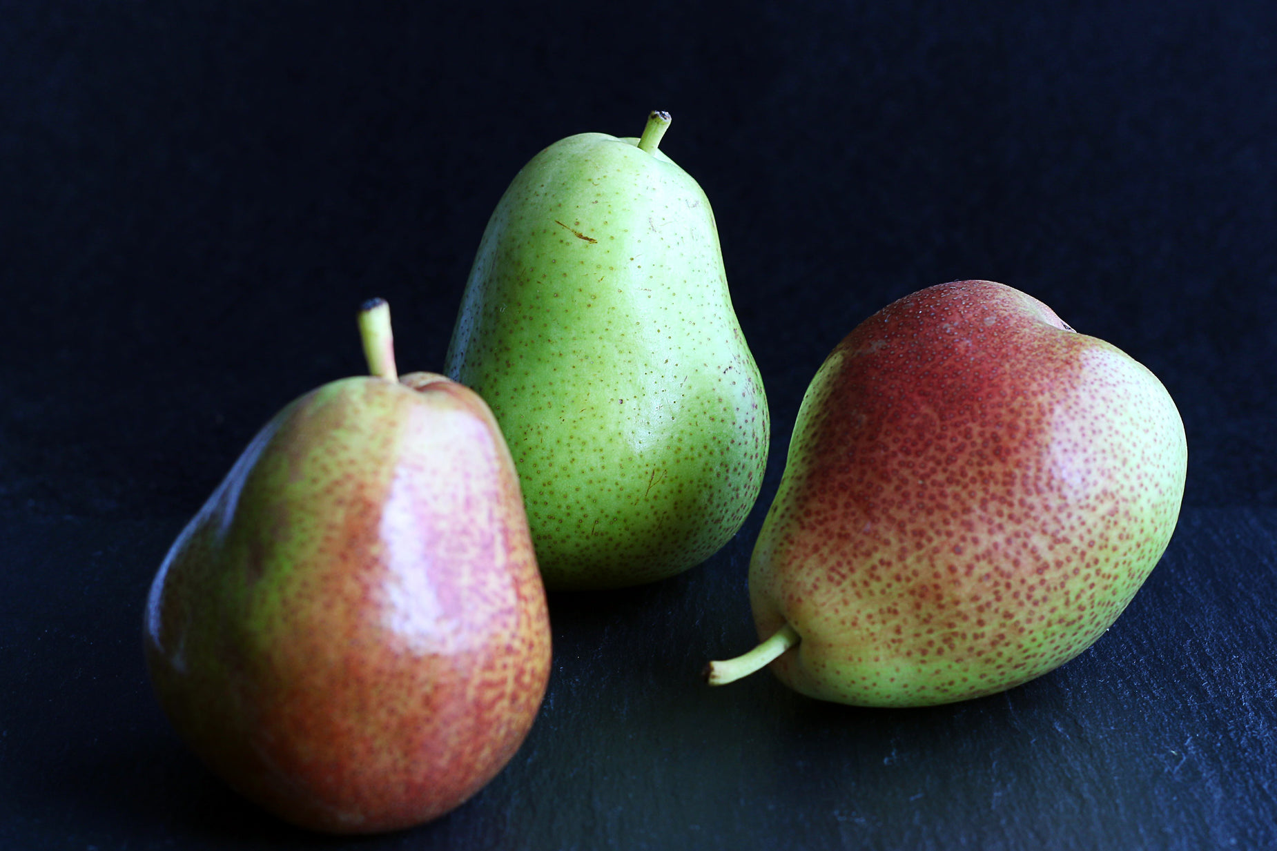 three green pears and one red pear are on a table