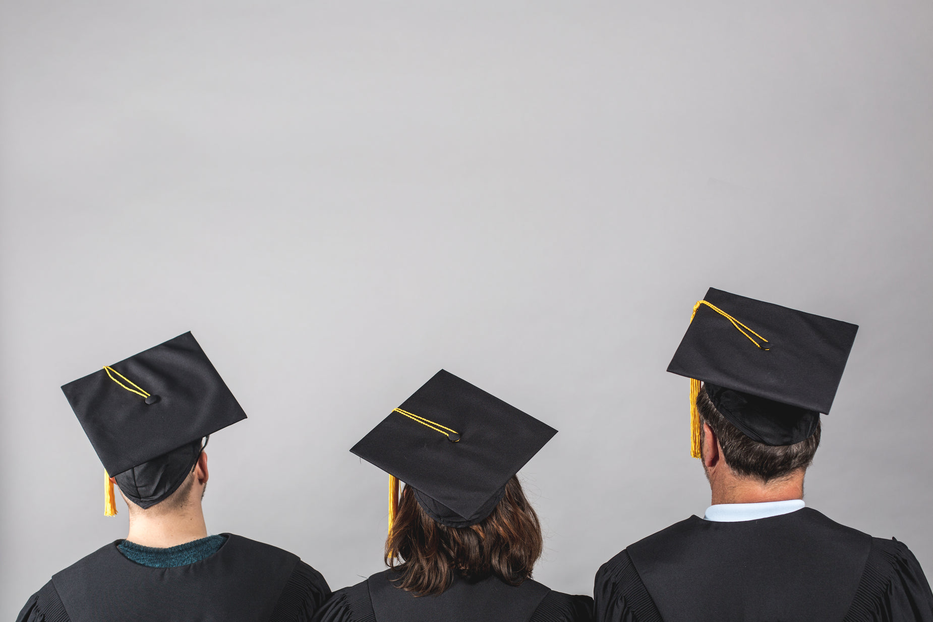 three graduates look toward the horizon in their graduation gowns