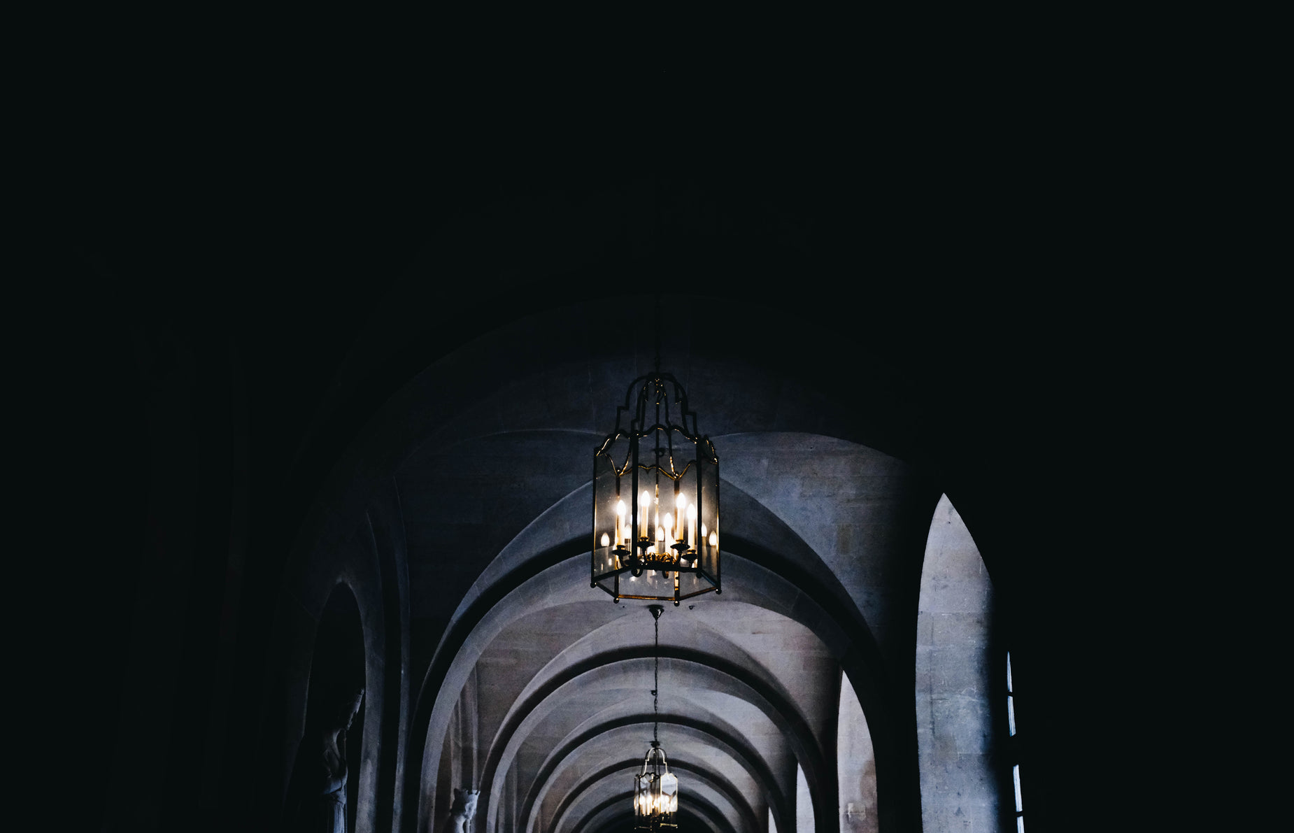 the long and narrow corridor has many arches, lights and columns