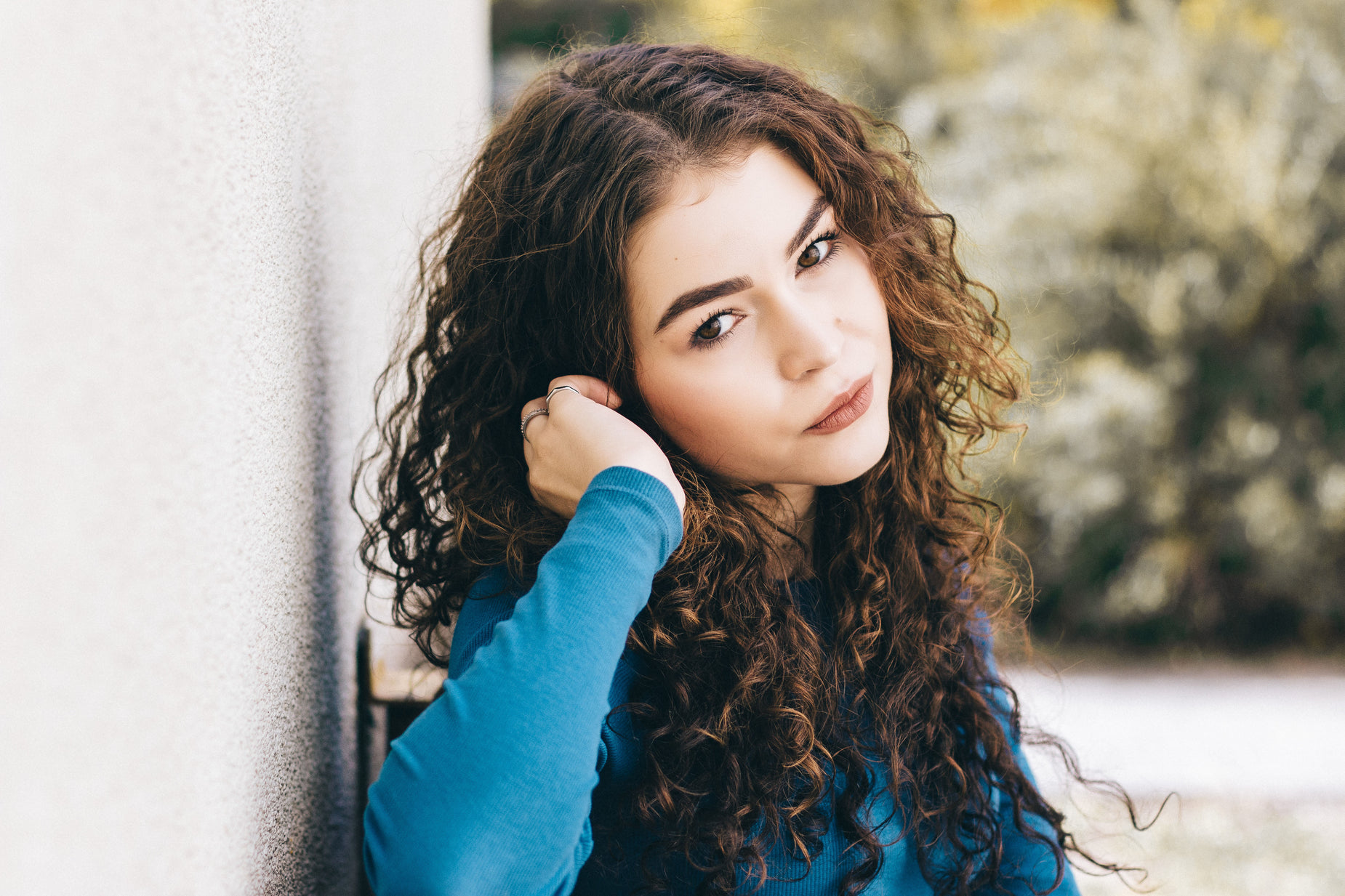 a girl with curly hair and blue shirt leaning against the wall