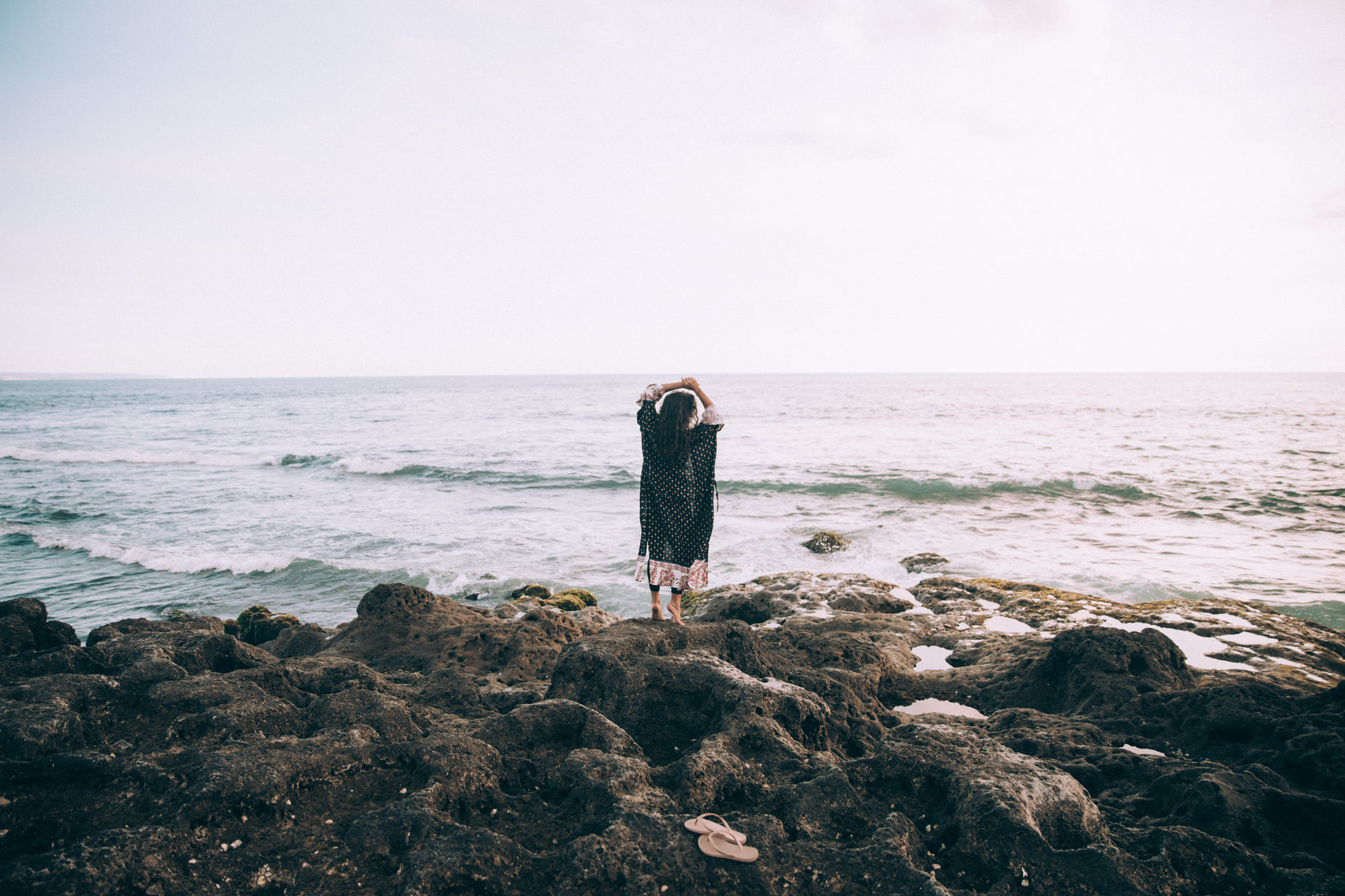 a woman with a hat stands on rocks over looking the water