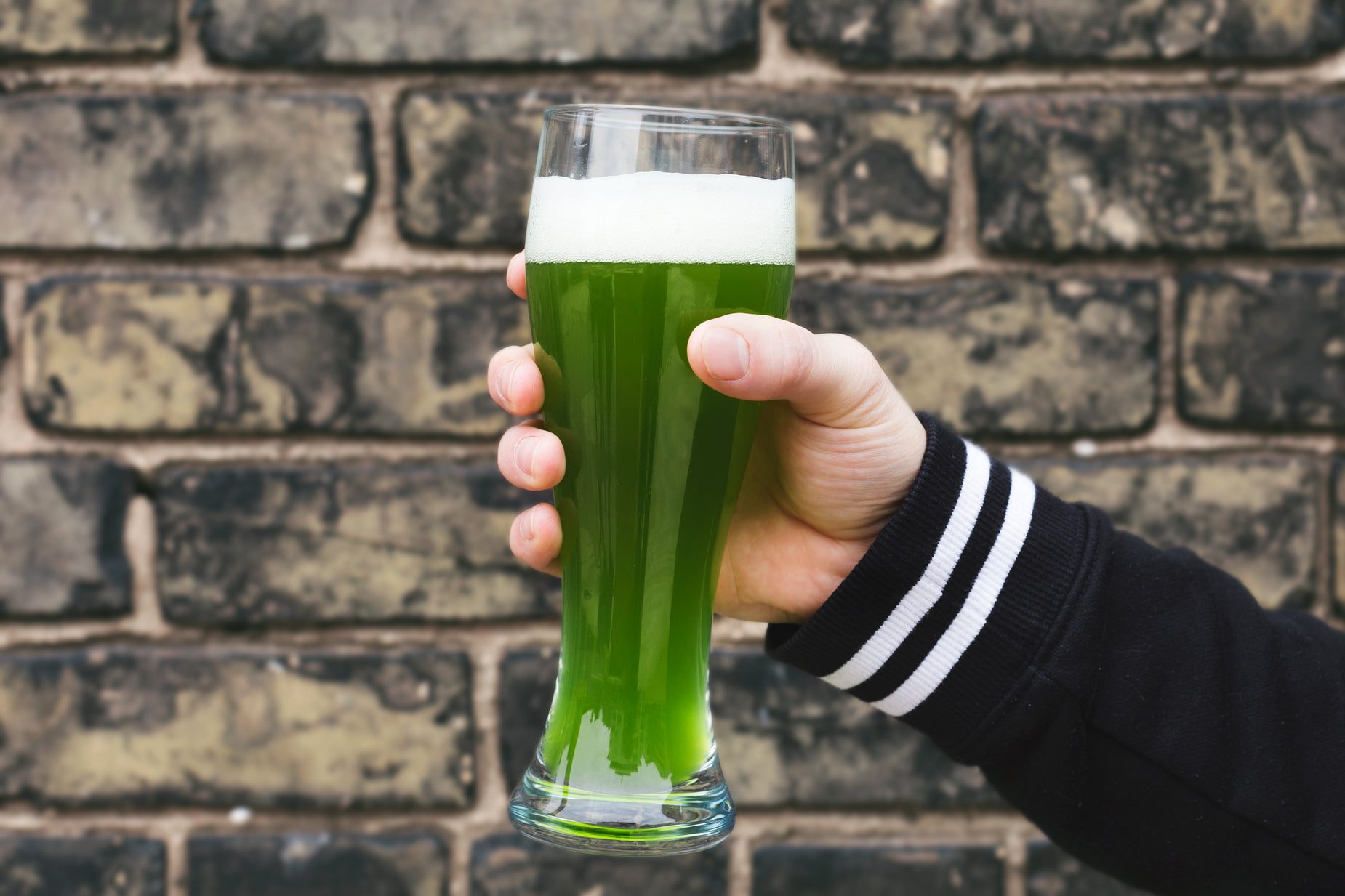 a man holds a glass filled with green liquid