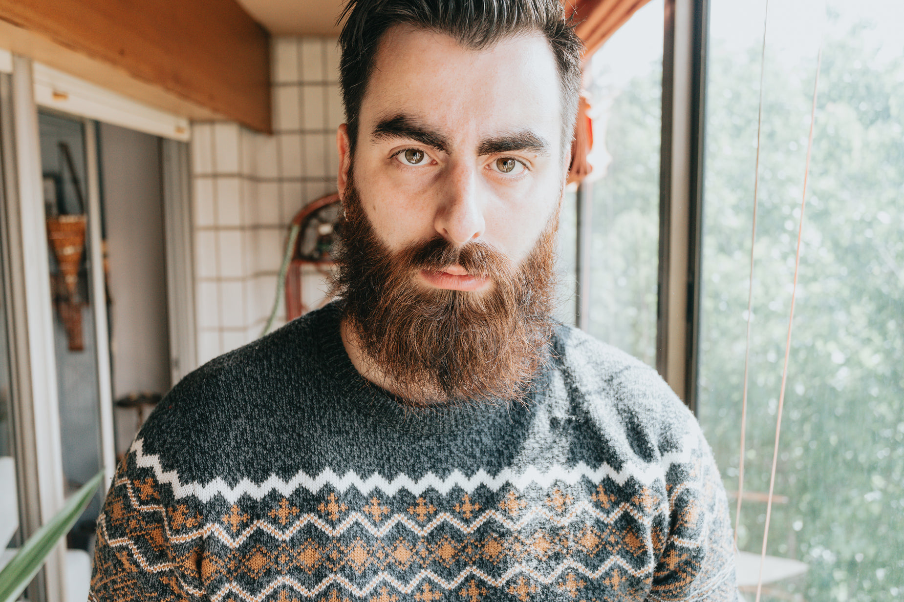 a man with a beard and patterned sweater looks intently ahead