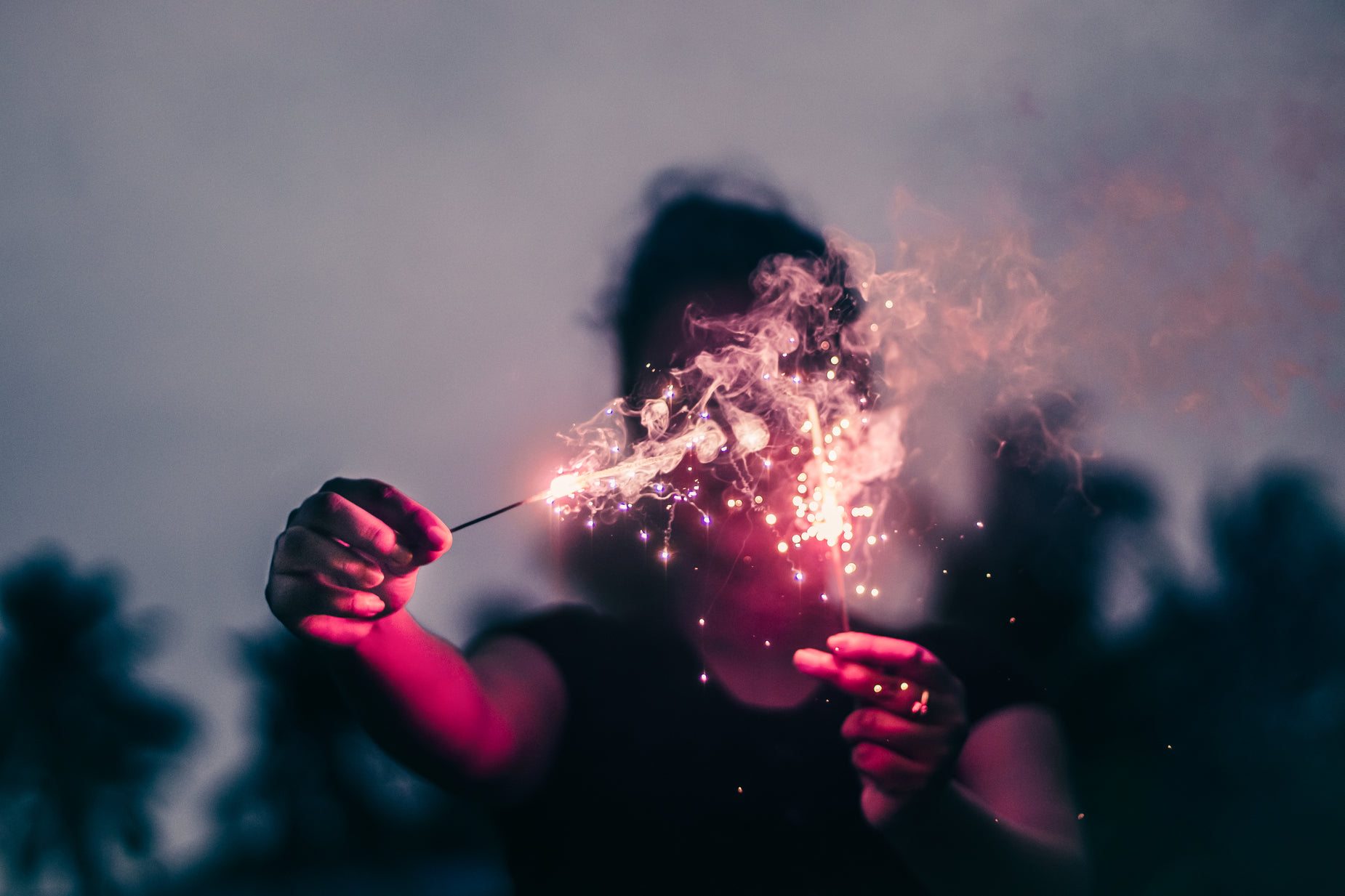the person is holding a sparkler with their face obscured by smoke