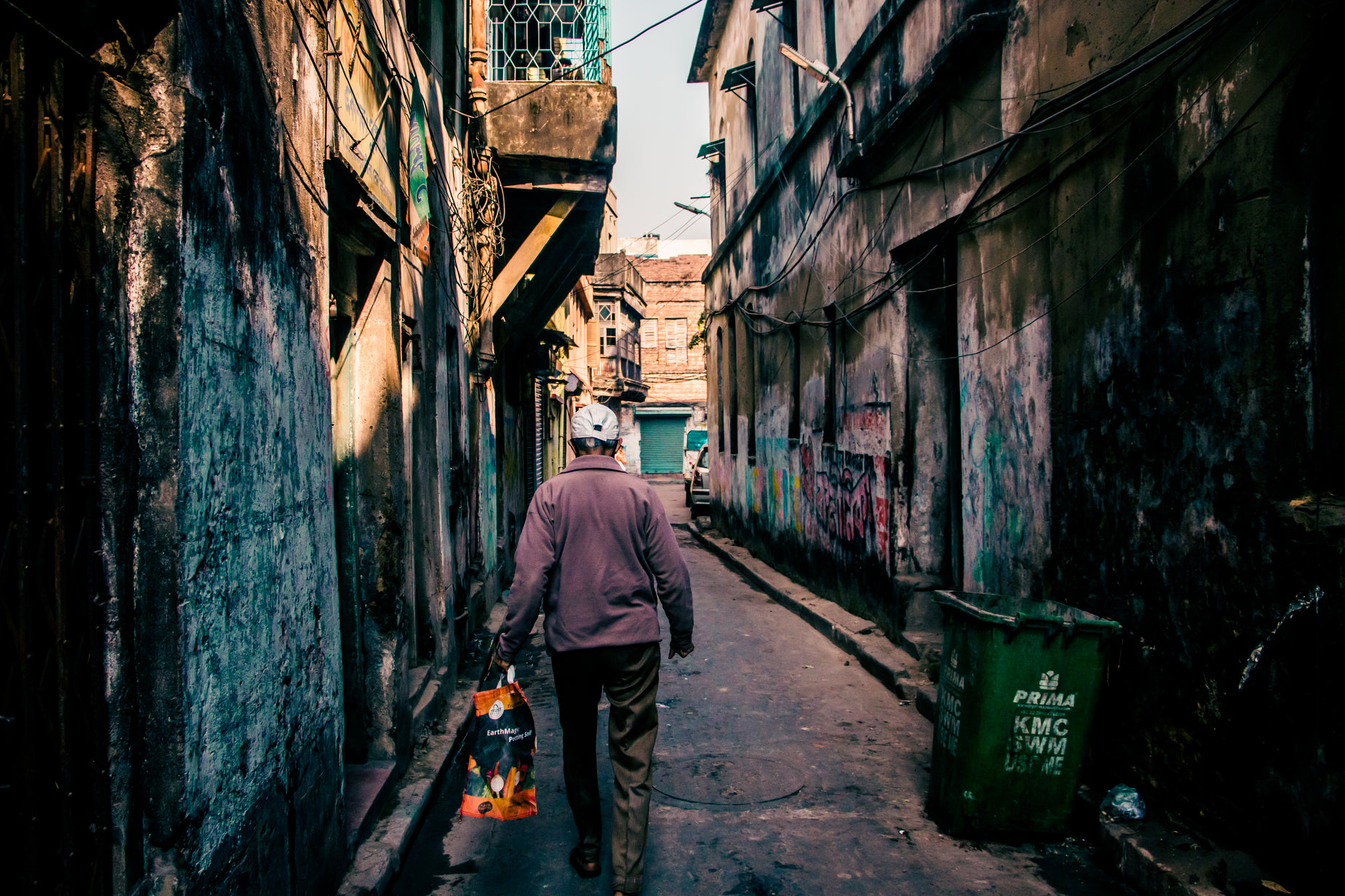 the man walks on a narrow alleyway with a bag