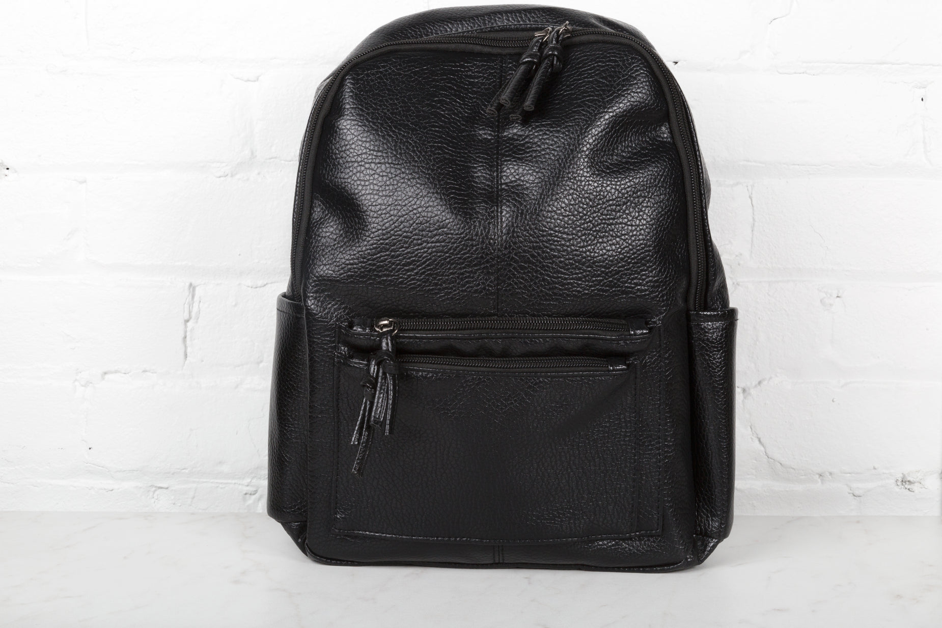 black backpack on the floor with white brick wall in background