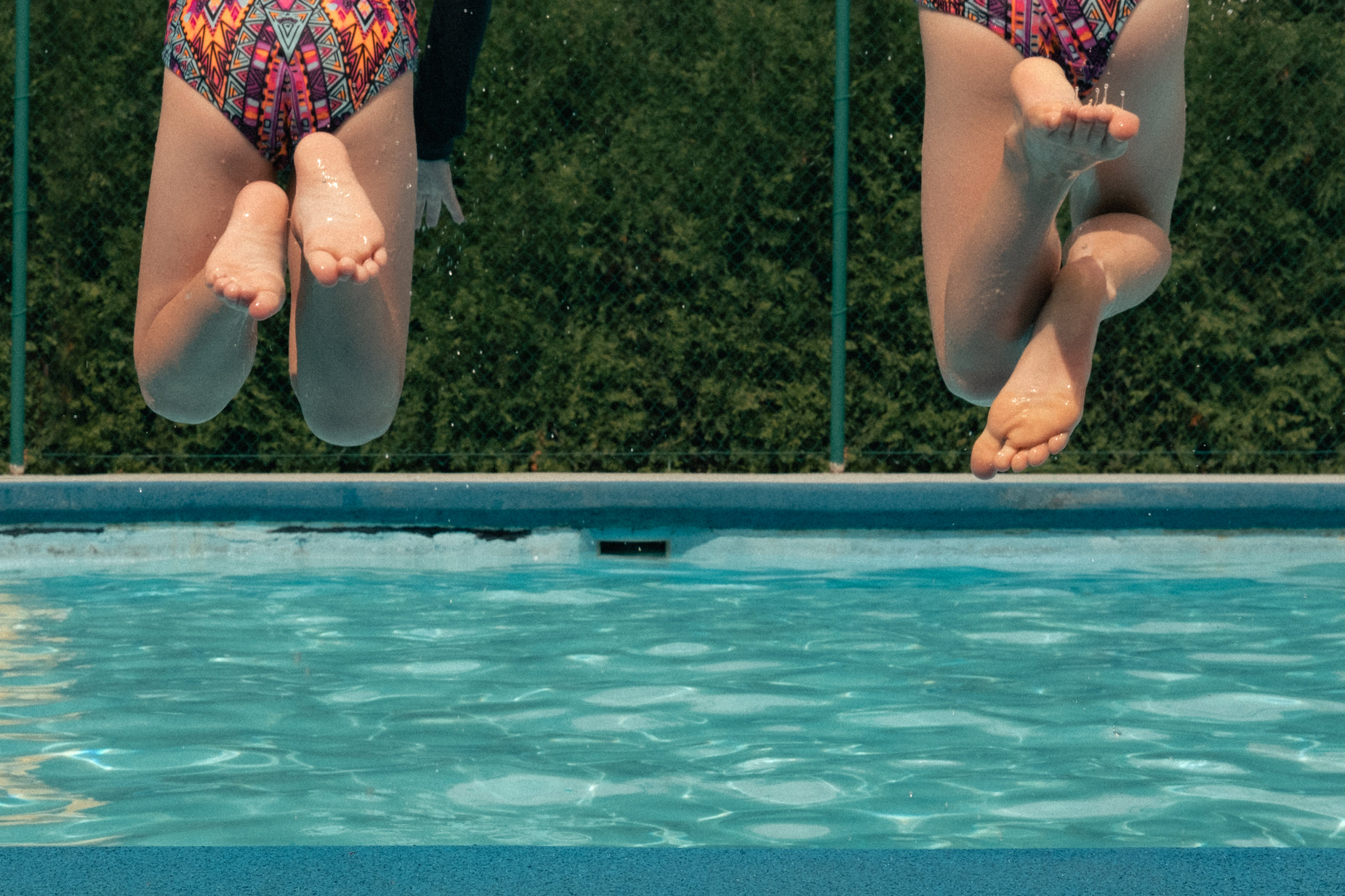 two girls jumping into the pool off the edge of their swim trunks