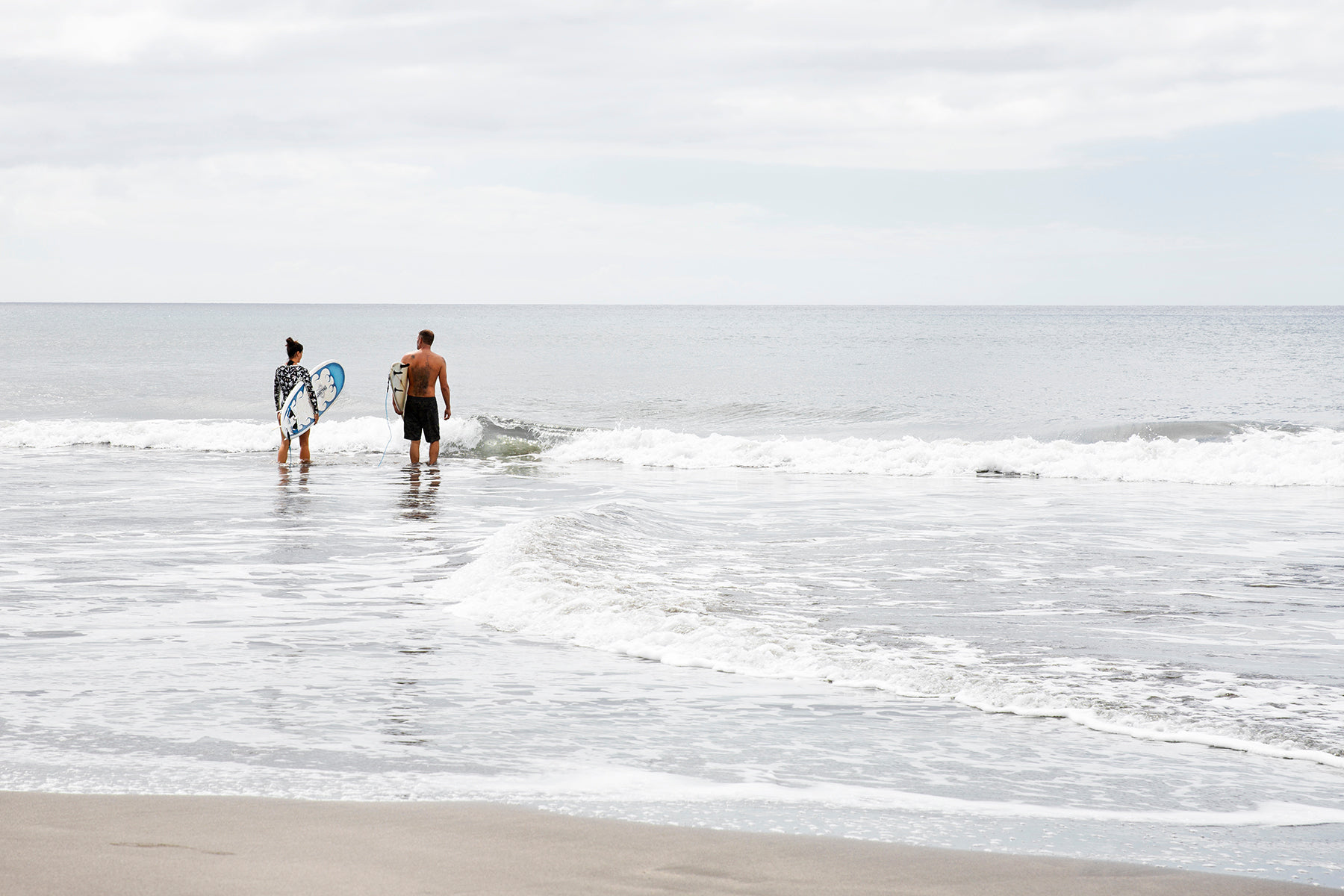 a man and woman walk out into the ocean with surfboards