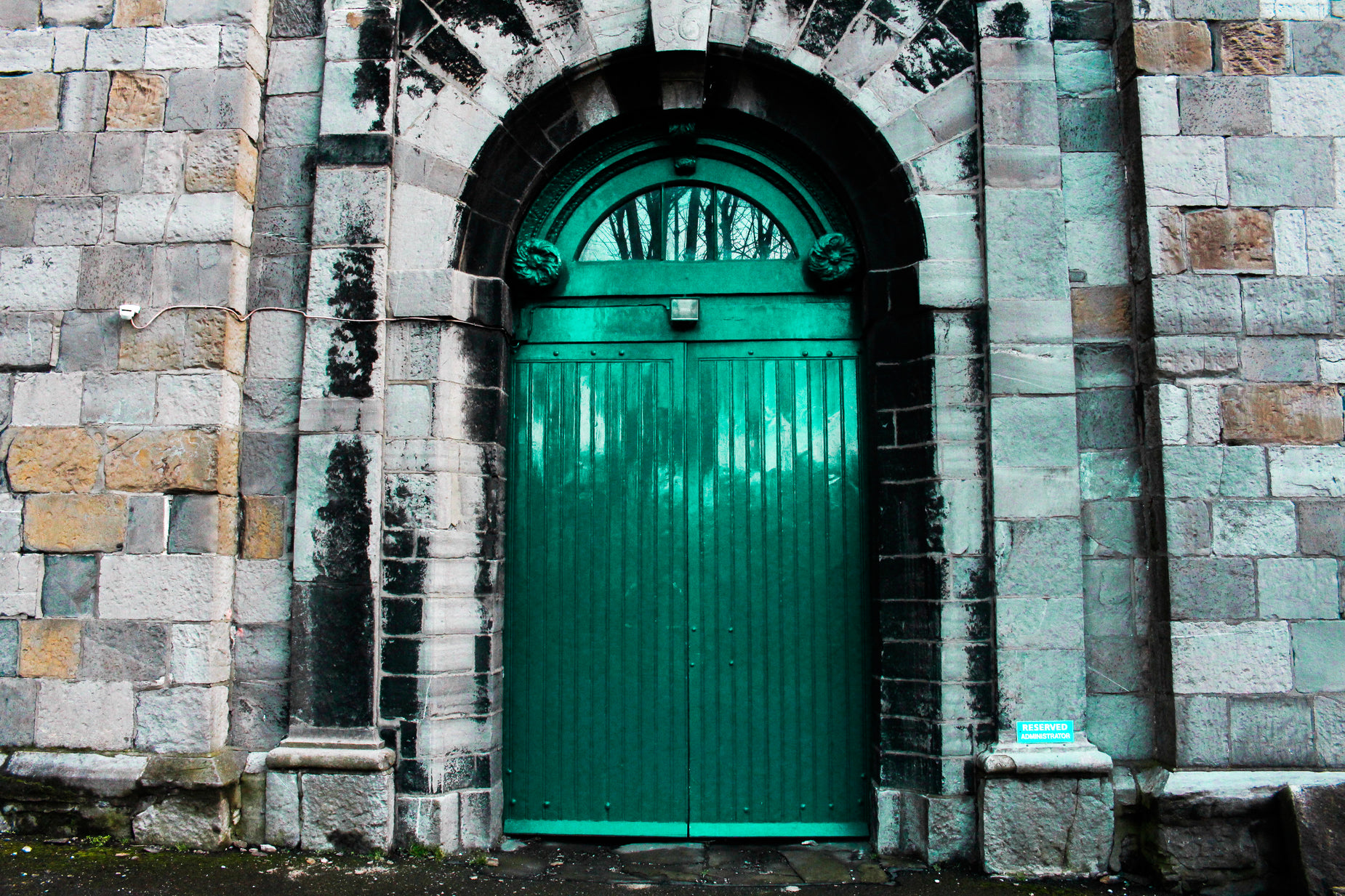 a green door with a large arched window next to a brick wall