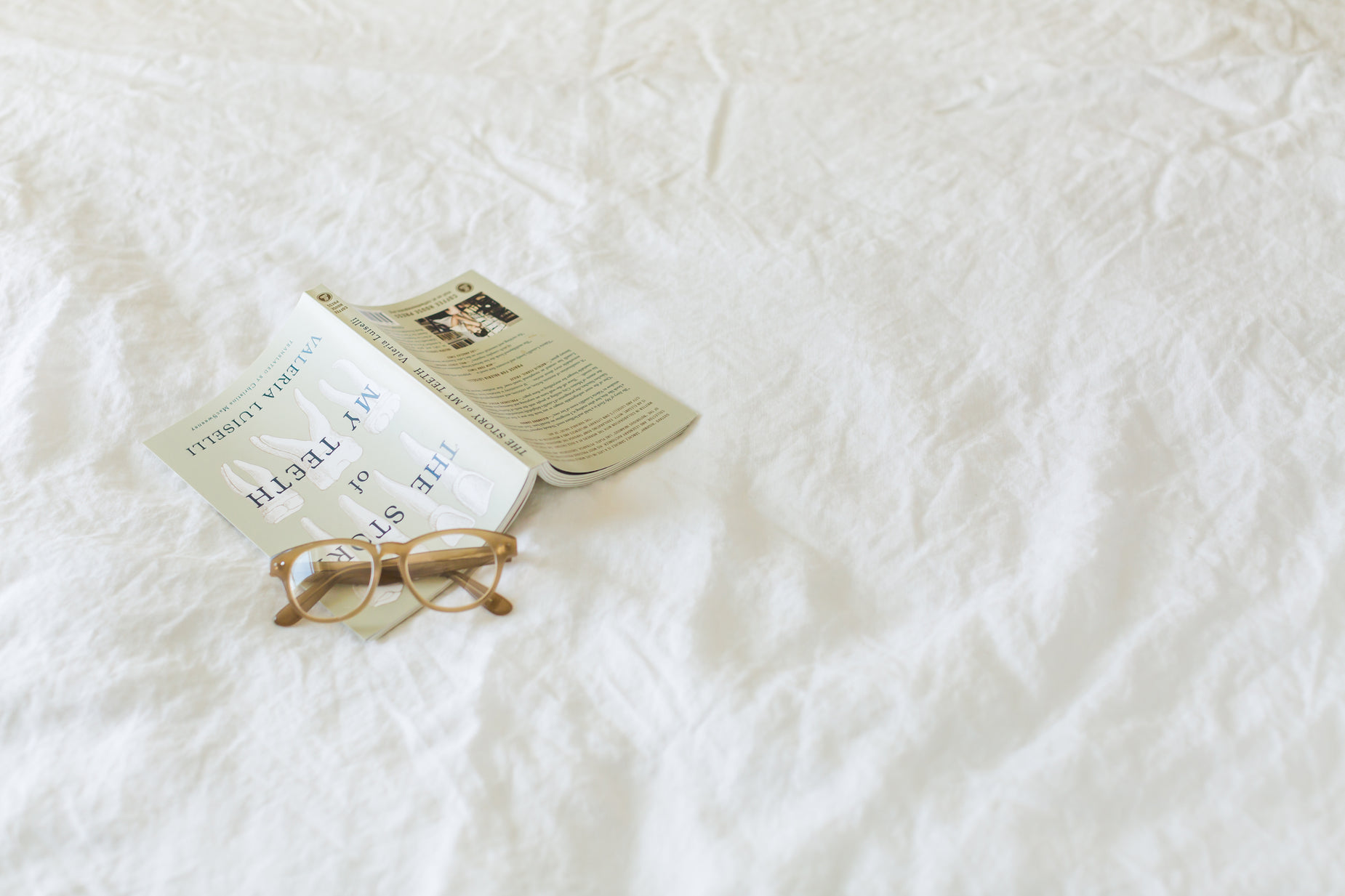 an open book on a bed next to reading glasses