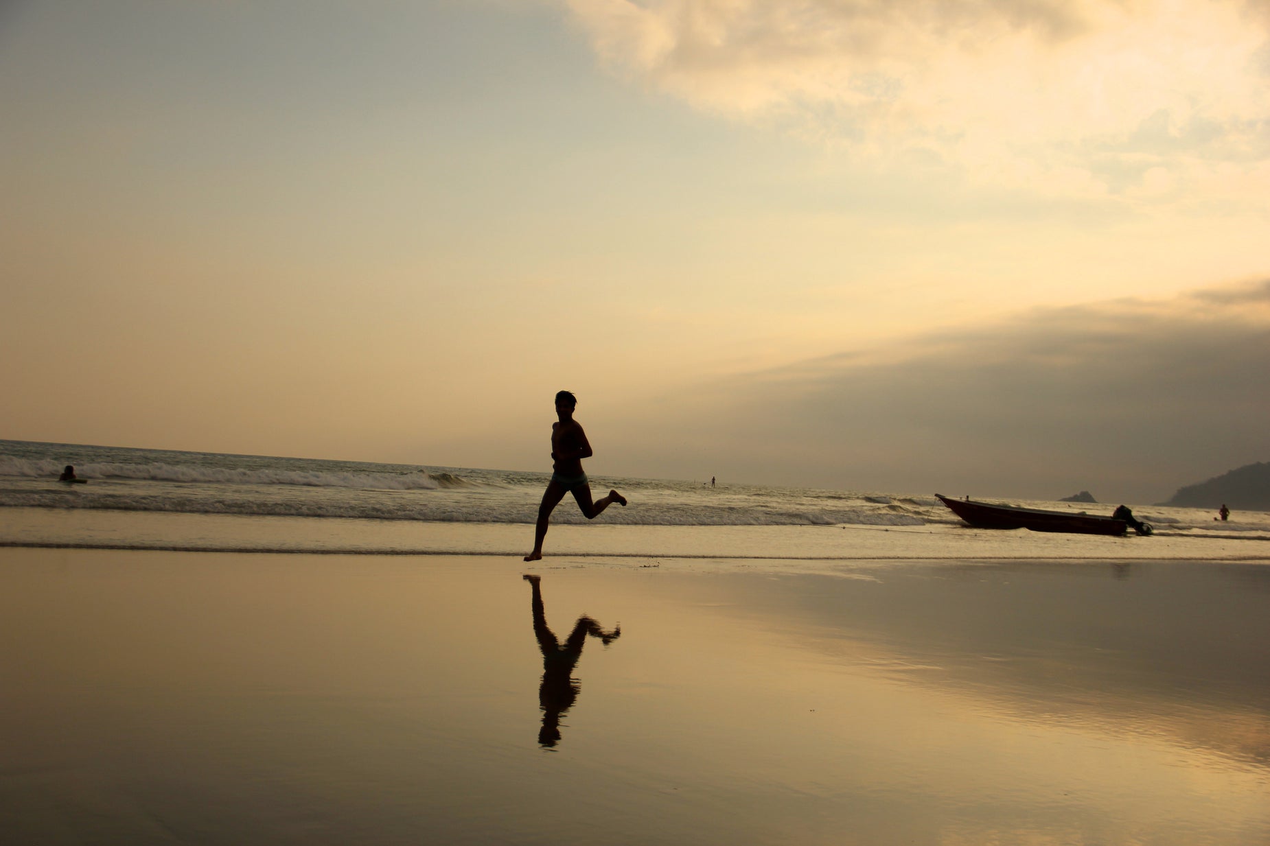 the man is running along the beach near a boat