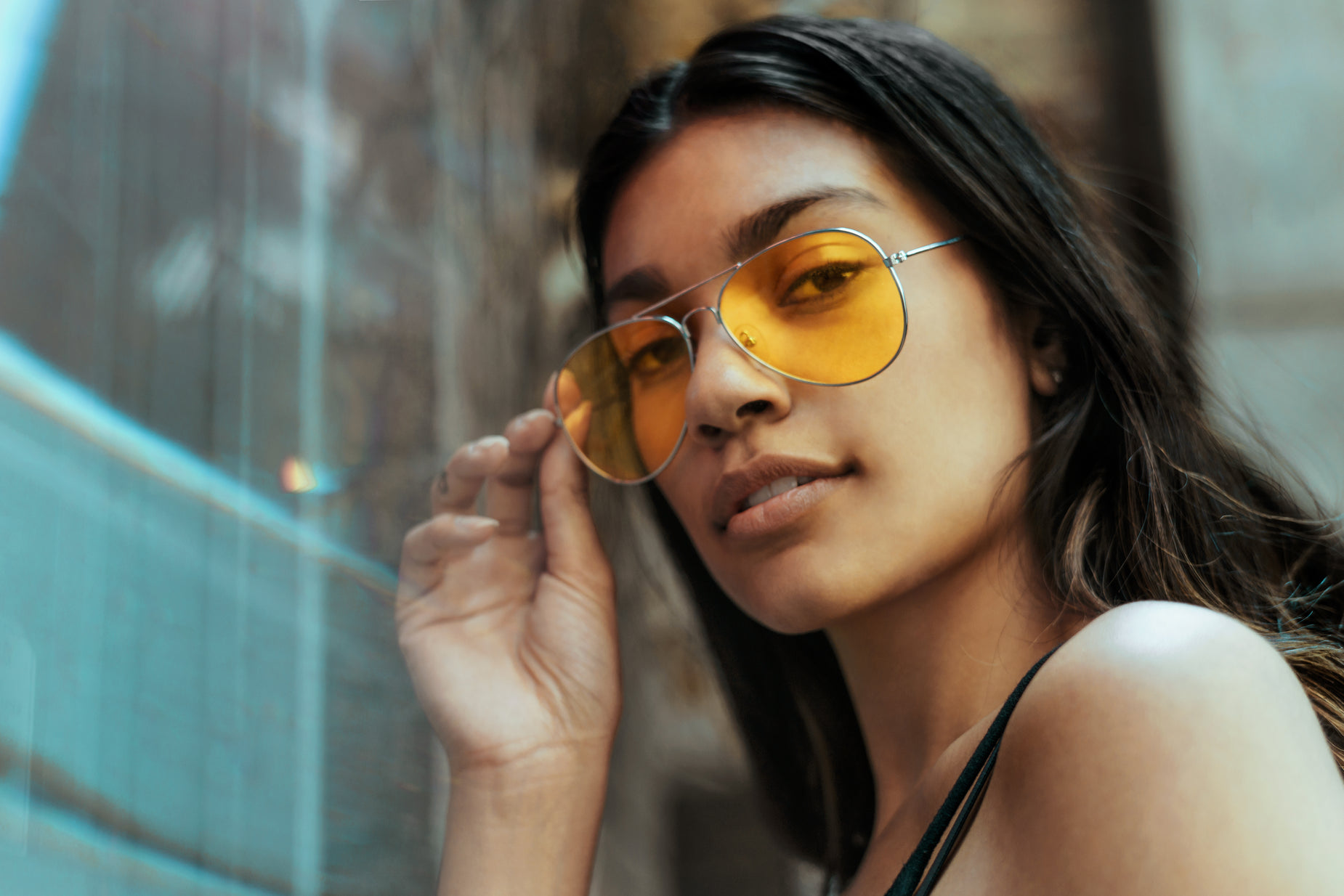 a woman in yellow sunglasses posing against a window