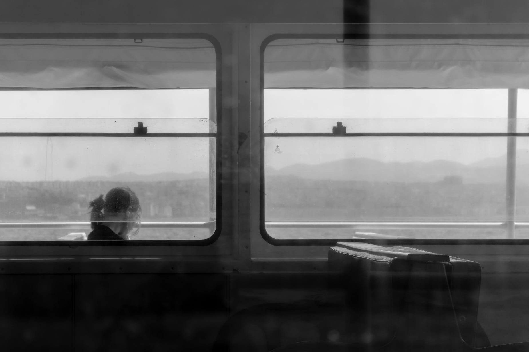 black and white pograph of a woman sitting on a bench on a train