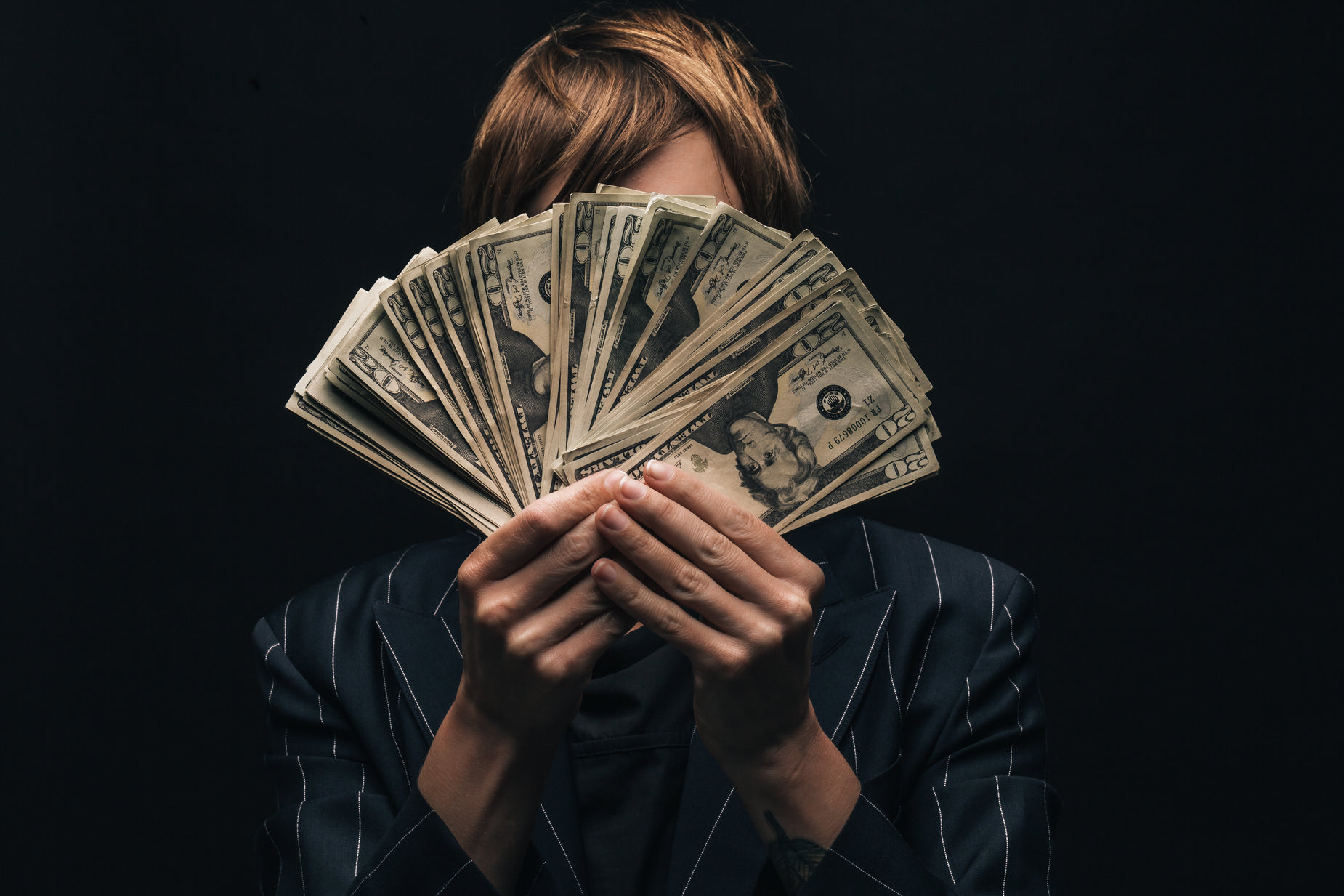 woman with her hands covering her face behind stacks of money