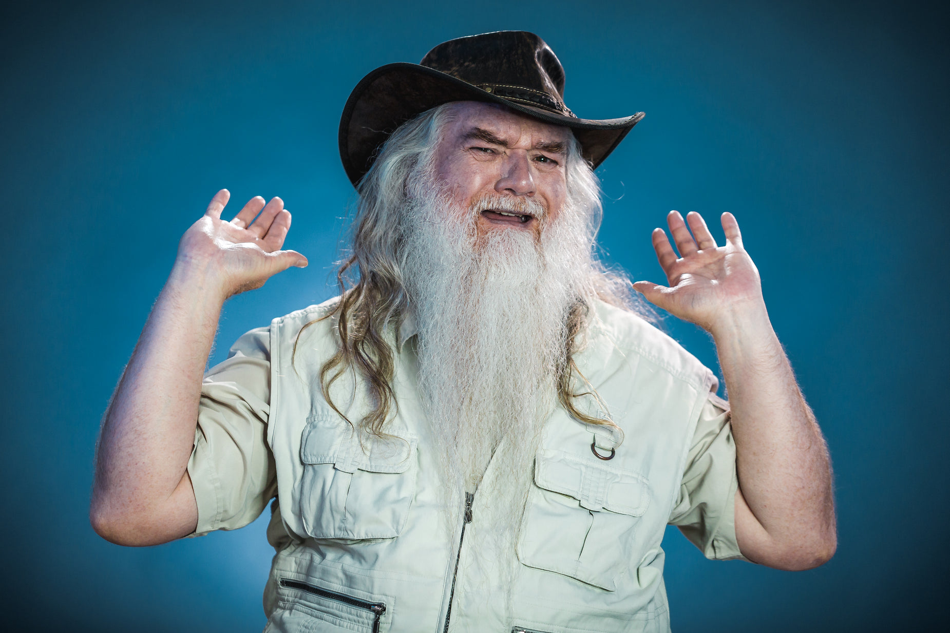 a bearded, man wearing a cowboy hat is making a hand sign