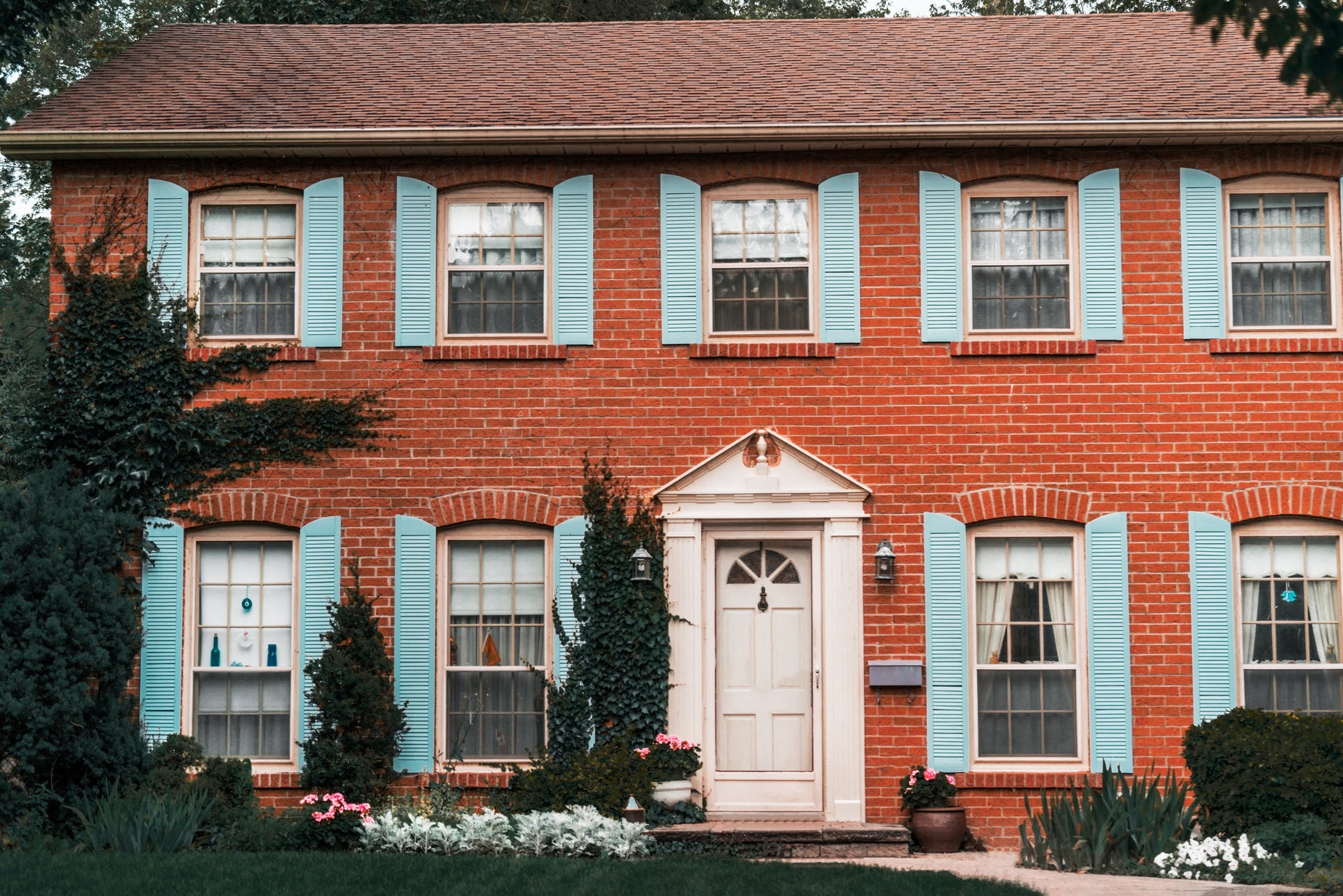 the exterior of a large red brick home with blue shutters