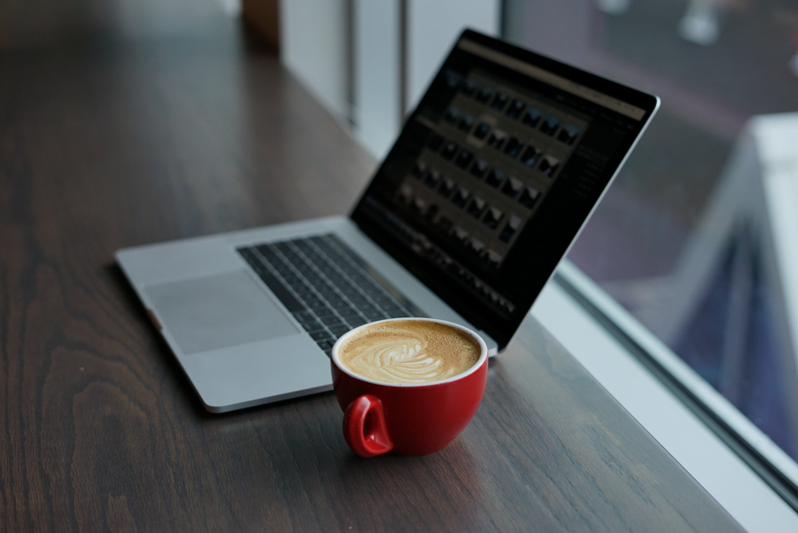 laptop and red cup on wooden desk with window