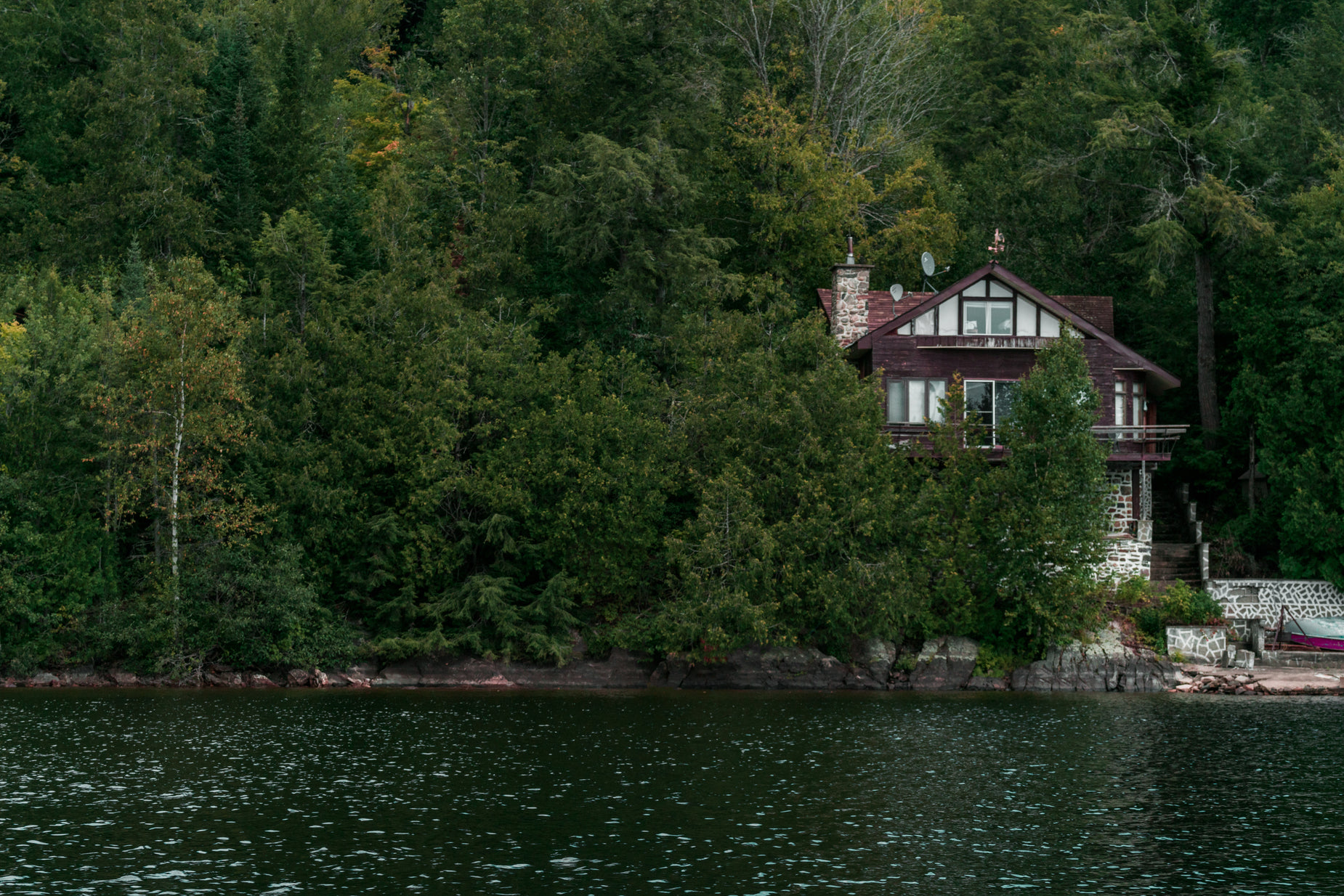 a large treed house on the shore near a lake