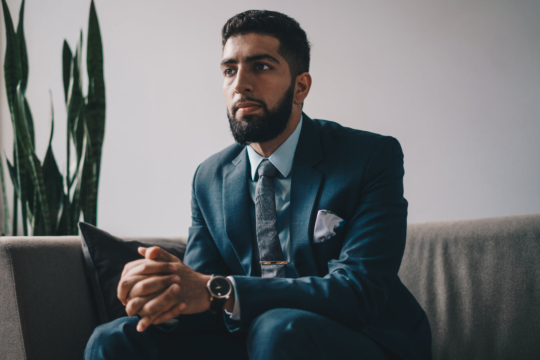 man wearing suit and tie looking ahead while sitting on a couch