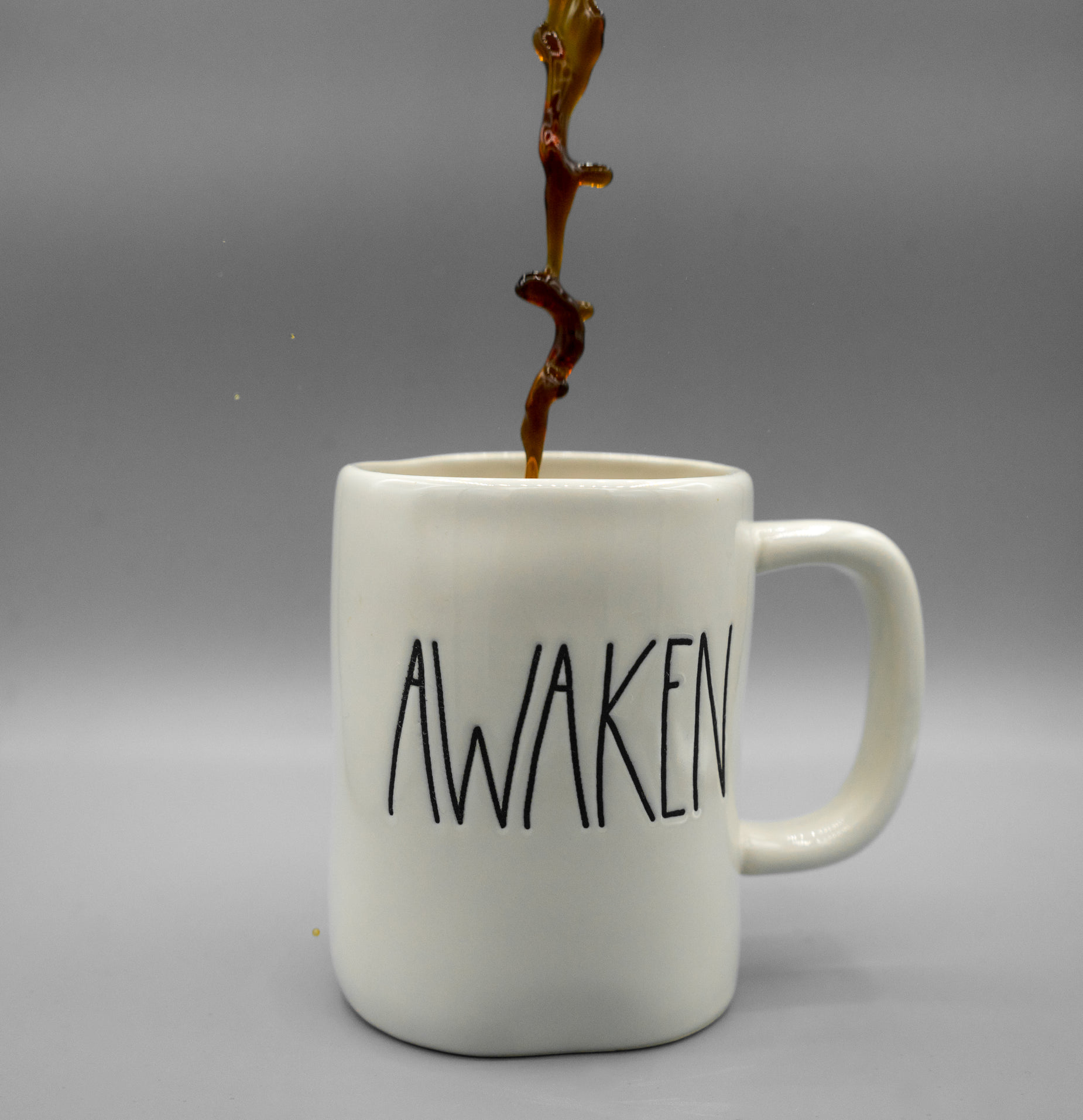 coffee is spilled into a ceramic cup with the word awaken