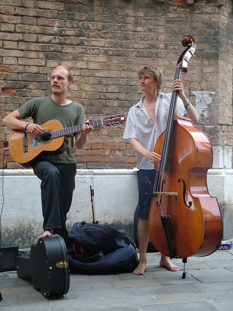 two musicians are on a sidewalk near the brick building