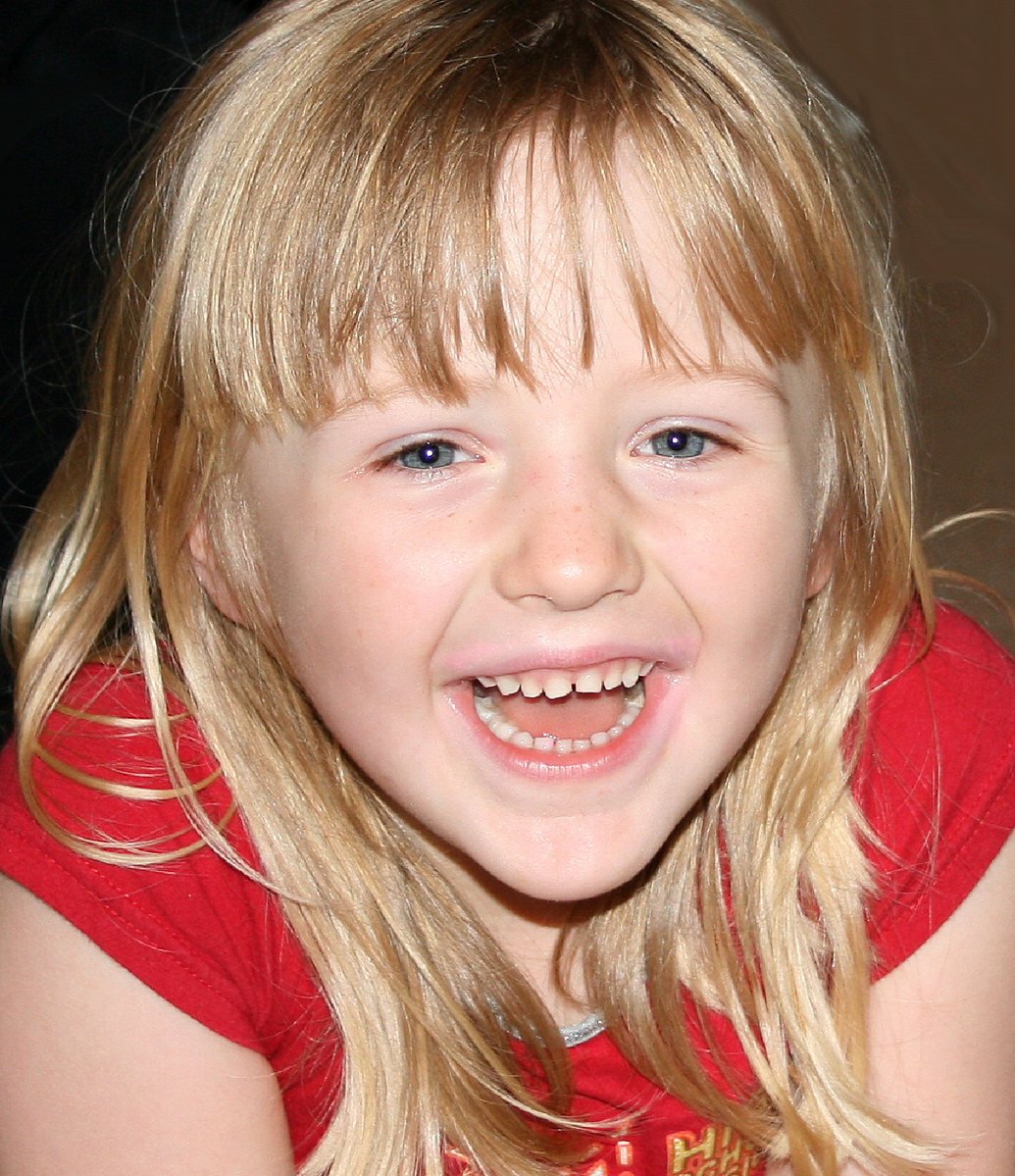 a child with blond hair, sitting on a couch smiling