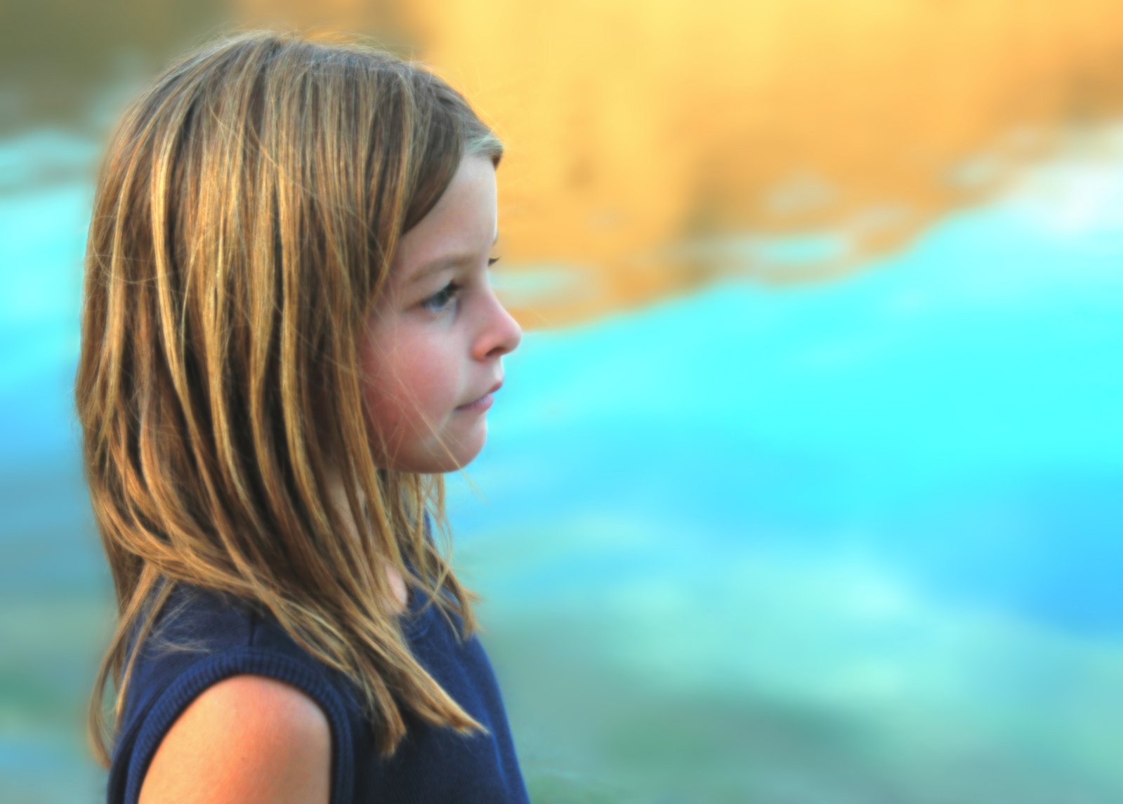 a little girl with long brown hair standing near a pond